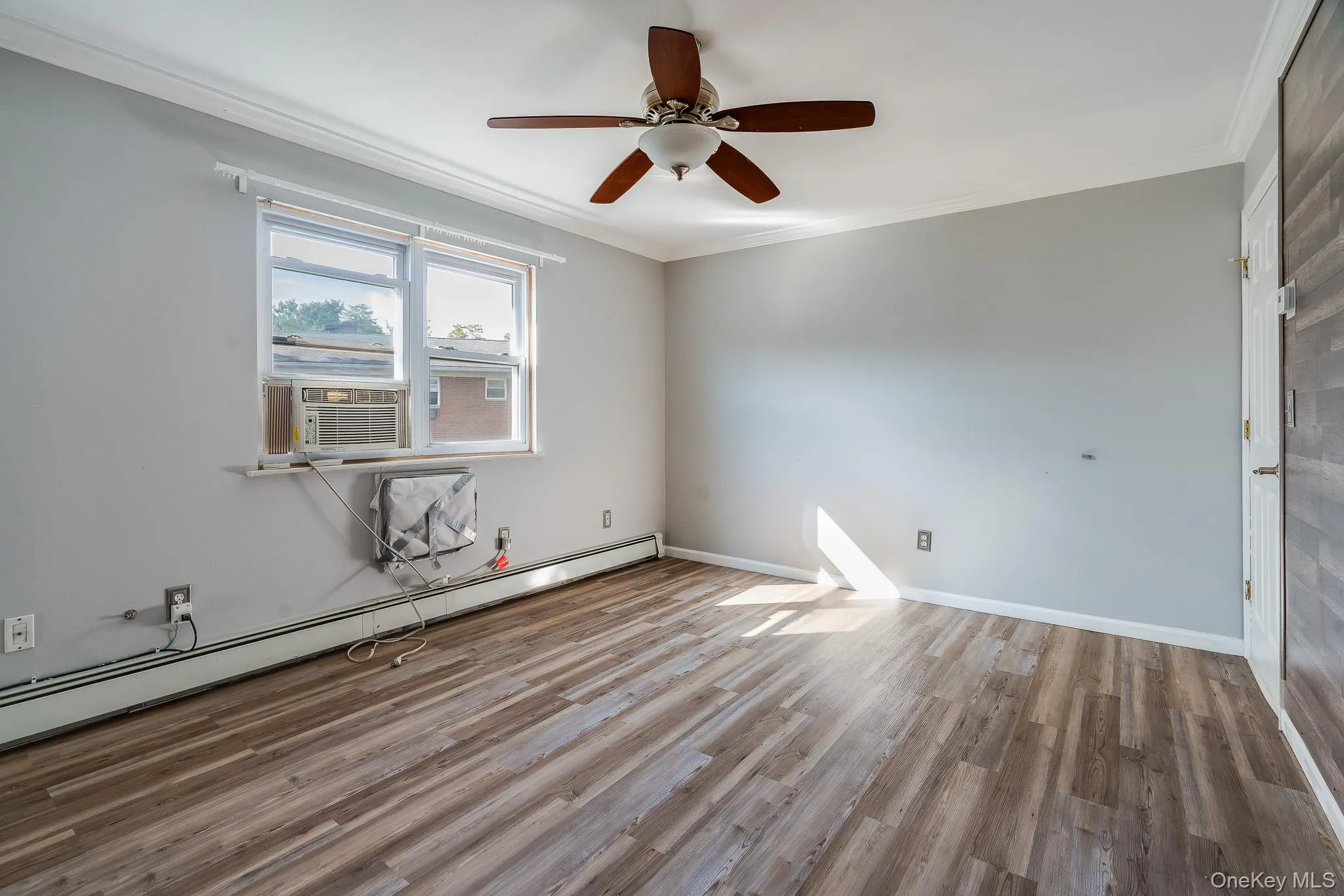Empty room with crown molding, a baseboard heating unit, light wood-style flooring, ceiling fan, and cooling unit Empty room with crown molding, a baseboard heating unit, light wood-style flooring, ceiling fan, and cooling unit