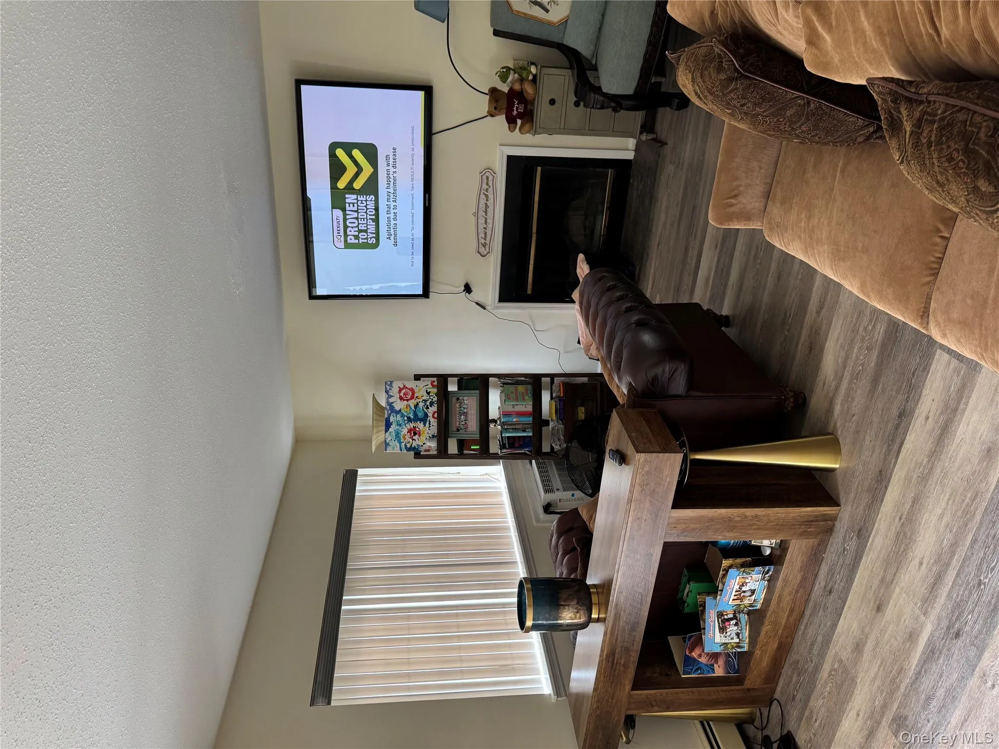 Living area with a fireplace with raised hearth, wood finished floors, a textured ceiling, and a baseboard heating unit Living area with a fireplace with raised hearth, wood finished floors, a textured ceiling, and a baseboard heating unit