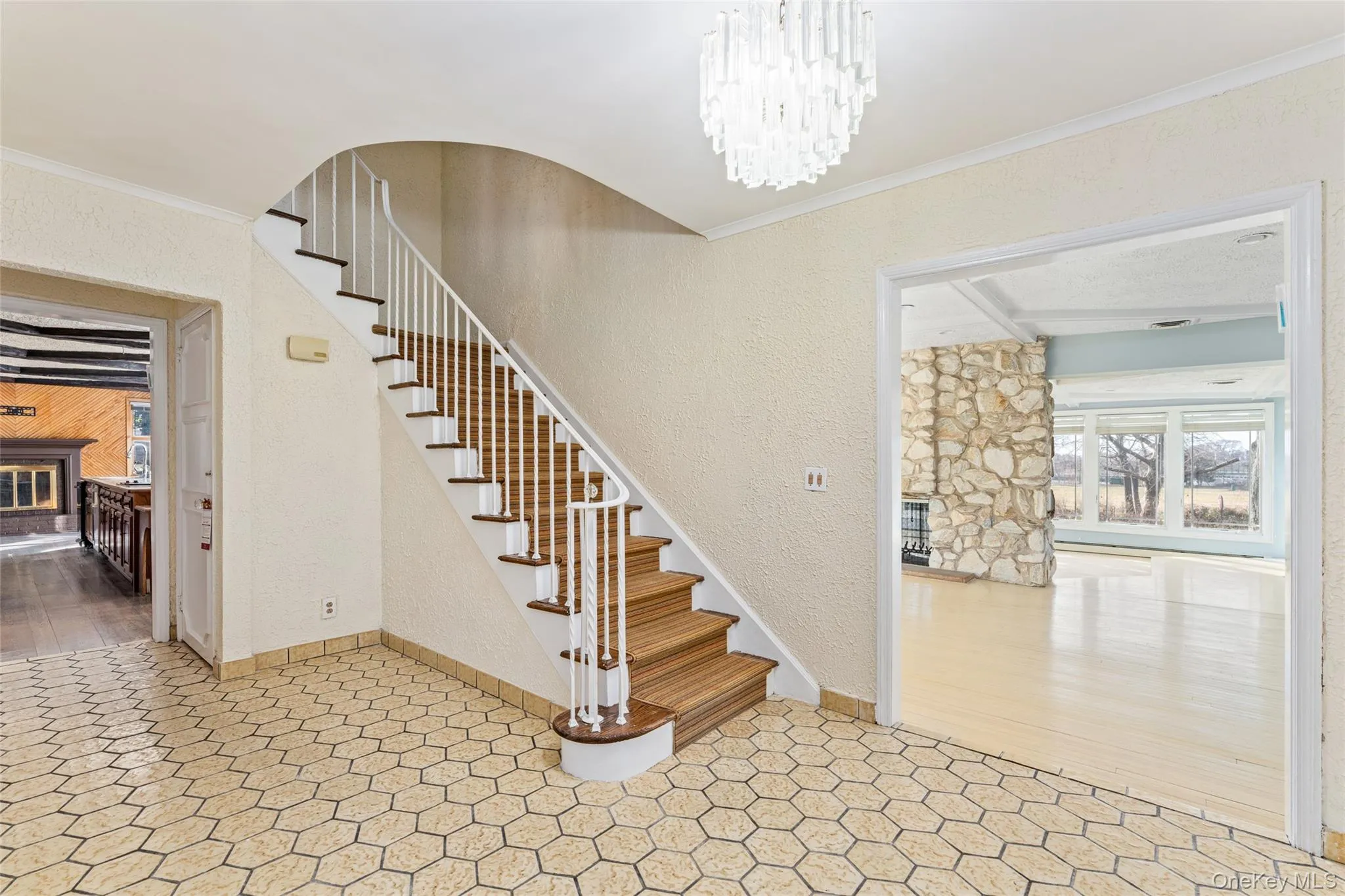 Stairs featuring a glass covered fireplace, a textured wall, a chandelier, crown molding, and beamed ceiling Stairs featuring a glass covered fireplace, a textured wall, a chandelier, crown molding, and beamed ceiling