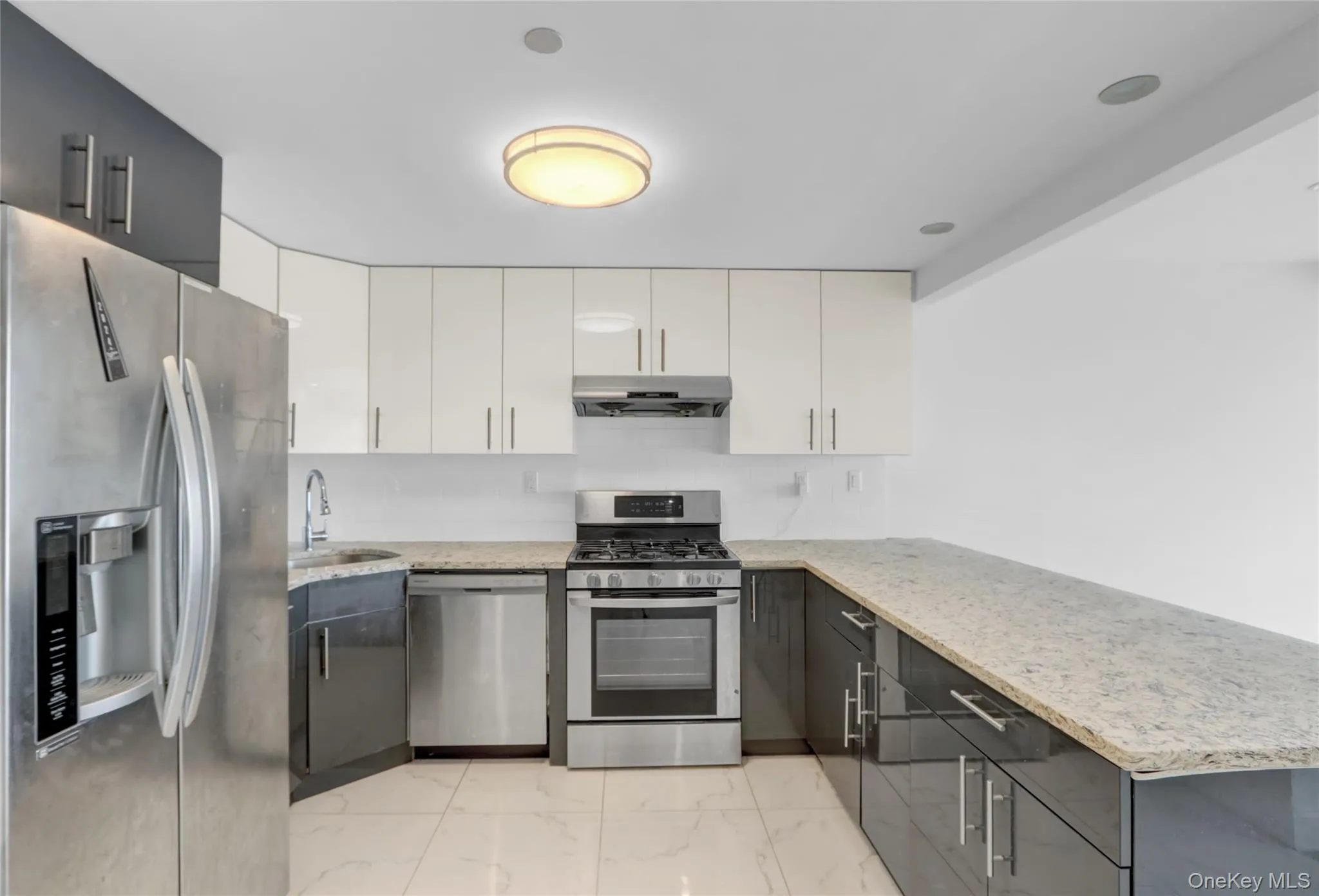 Kitchen with stainless steel appliances, light stone countertops, light marble finish flooring, and white cabinetry Kitchen with stainless steel appliances, light stone countertops, light marble finish flooring, and white cabinetry