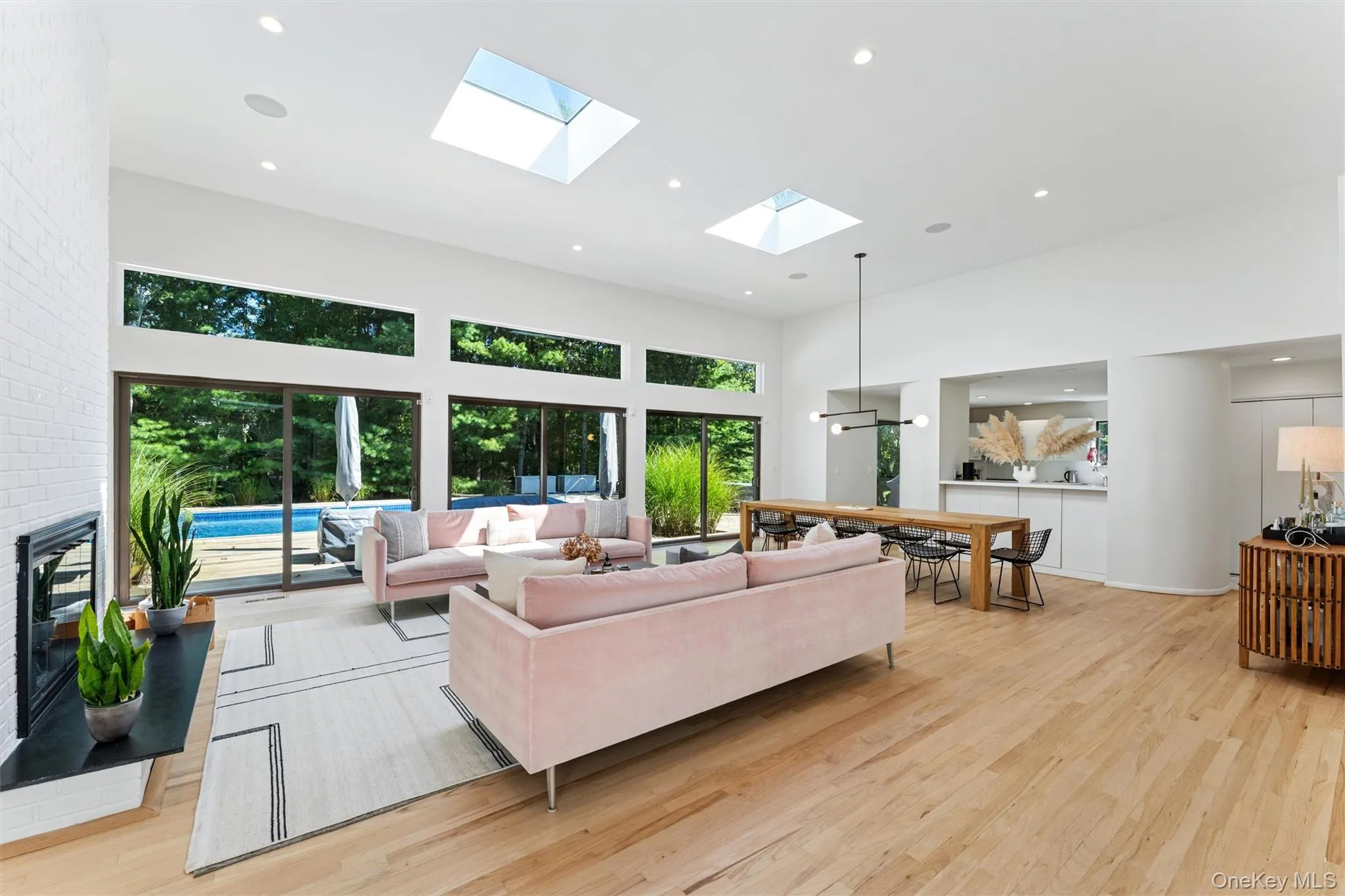 Living room featuring recessed lighting, a towering ceiling, light wood-style flooring, plenty of natural light, and a skylight Living room featuring recessed lighting, a towering ceiling, light wood-style flooring, plenty of natural light, and a skylight