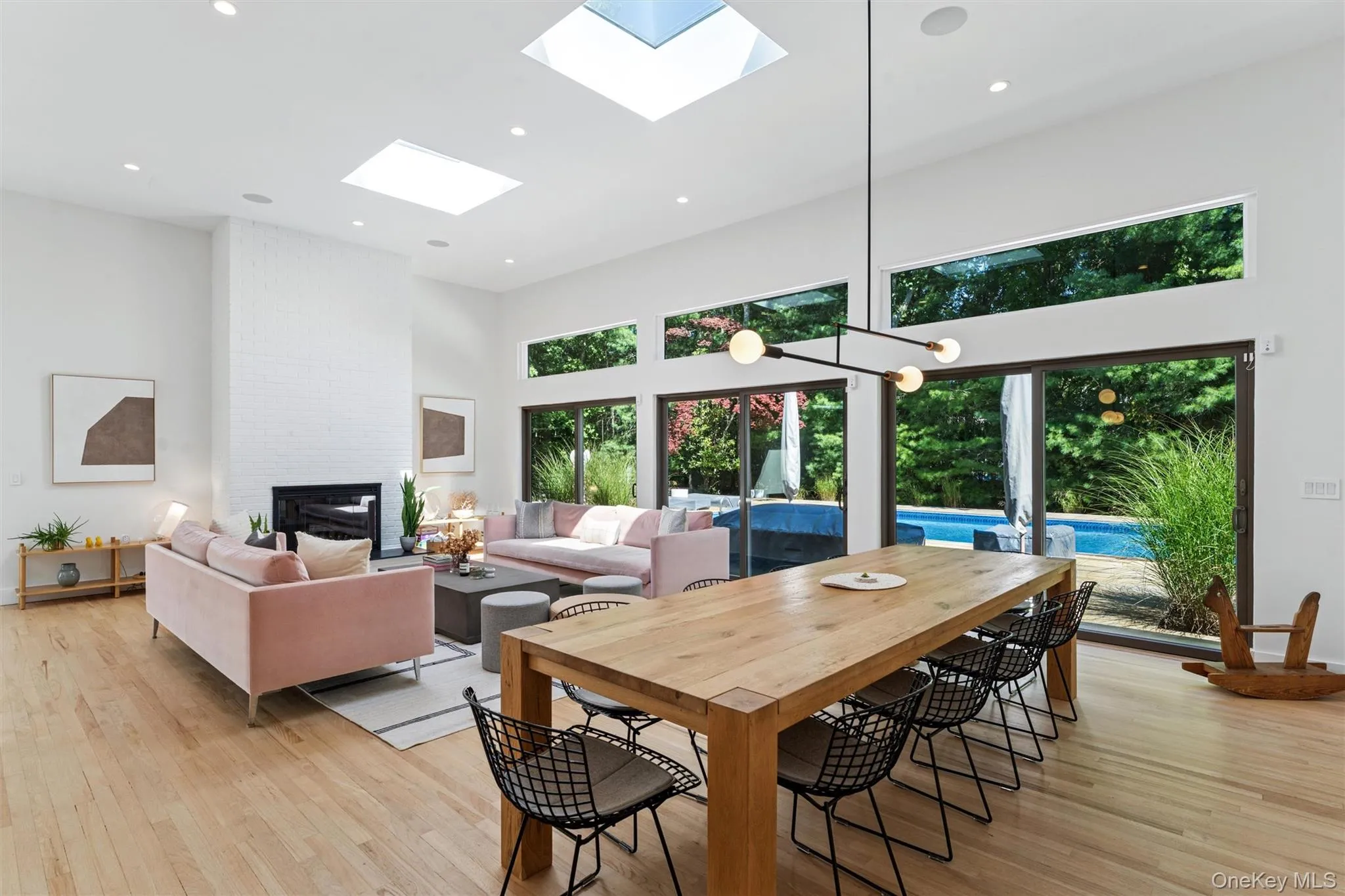 Dining room featuring a towering ceiling, a brick fireplace, light wood finished floors, recessed lighting, and a skylight Dining room featuring a towering ceiling, a brick fireplace, light wood finished floors, recessed lighting, and a skylight
