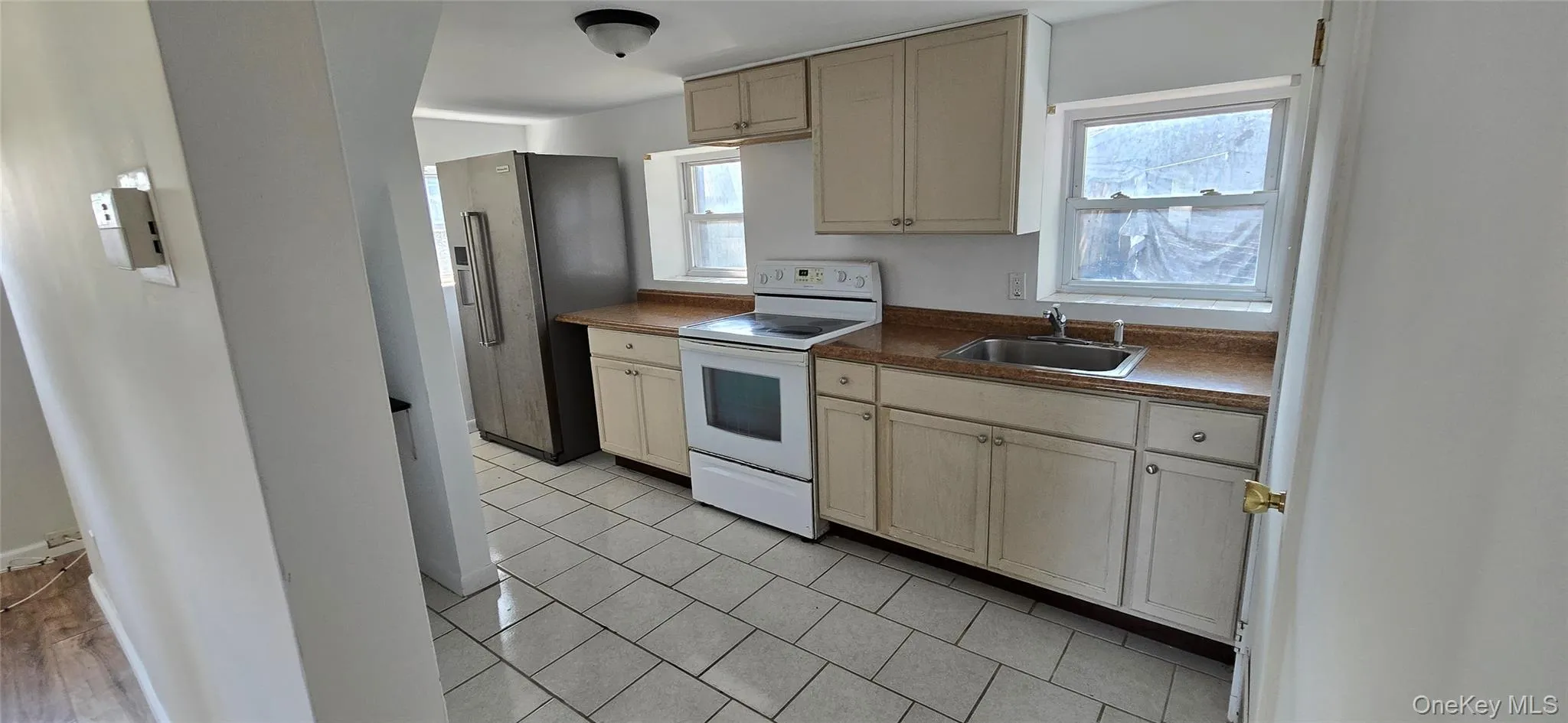 Kitchen with electric range, stainless steel refrigerator with ice dispenser, dark countertops, light tile patterned flooring, and cream cabinetry Kitchen with electric range, stainless steel refrigerator with ice dispenser, dark countertops, light tile patterned flooring, and cream cabinetry