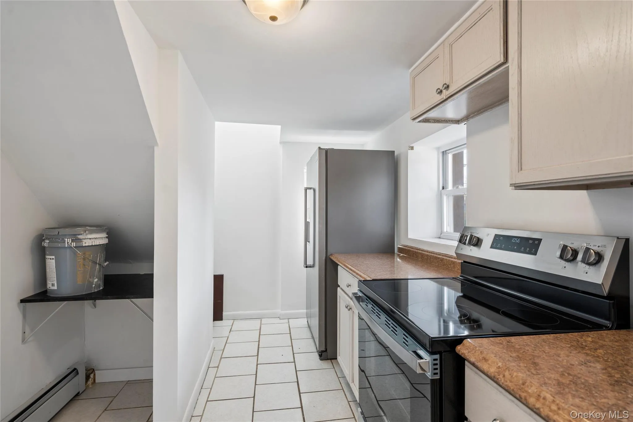 Kitchen featuring stainless steel appliances, a baseboard radiator, dark countertops, and light tile patterned floors Kitchen featuring stainless steel appliances, a baseboard radiator, dark countertops, and light tile patterned floors