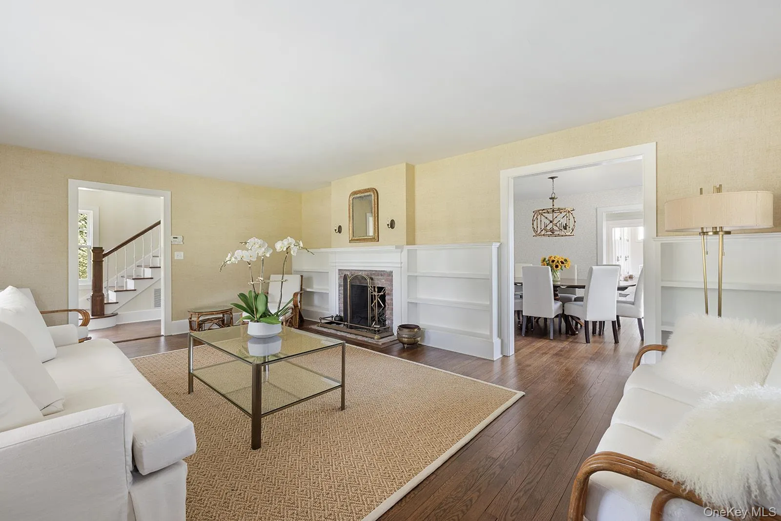 Living room with dark wood-style floors, a brick fireplace, wallpapered walls, and stairway Living room with dark wood-style floors, a brick fireplace, wallpapered walls, and stairway