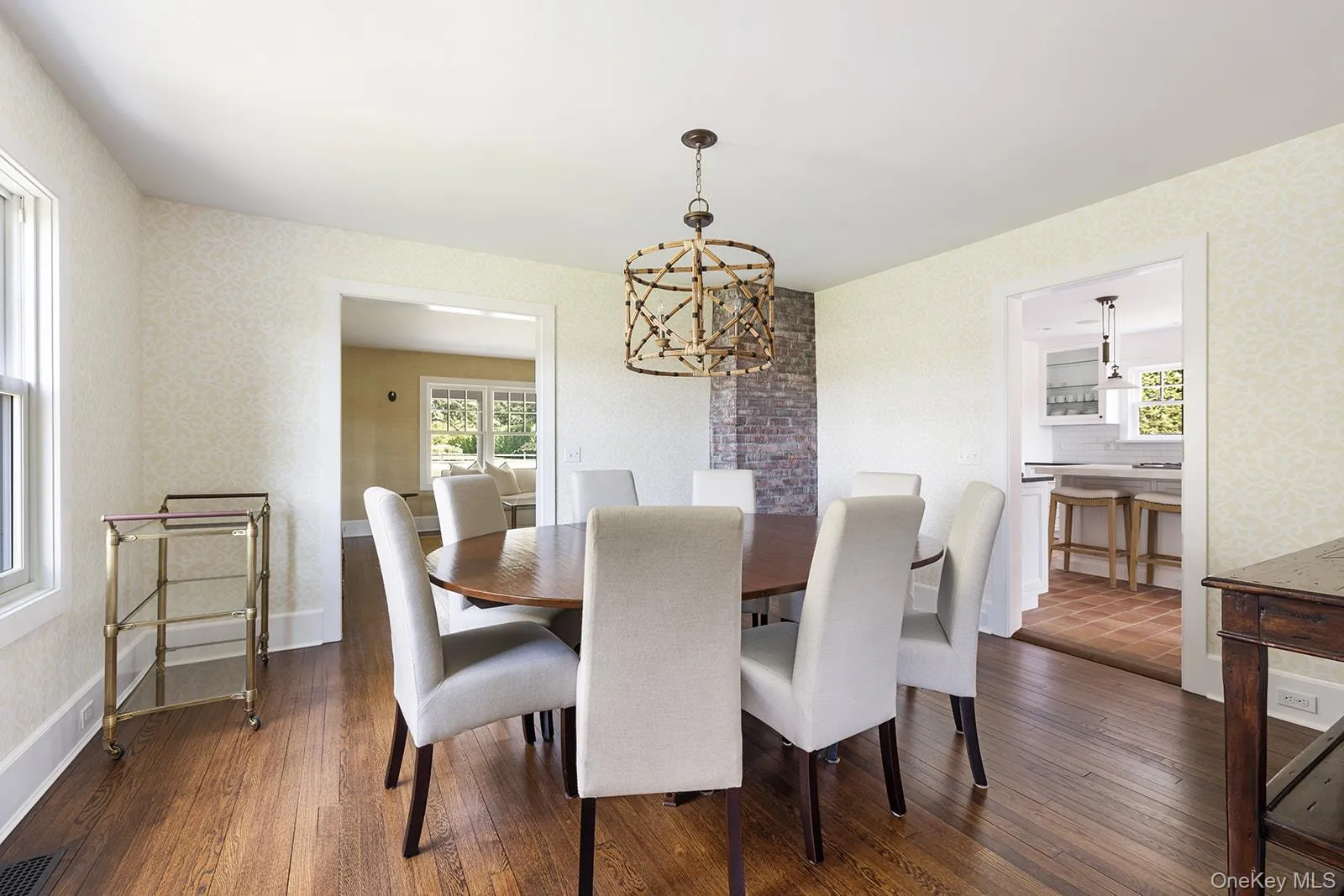 Dining room with dark wood-style floors, a chandelier, wallpapered walls, and plenty of natural light Dining room with dark wood-style floors, a chandelier, wallpapered walls, and plenty of natural light