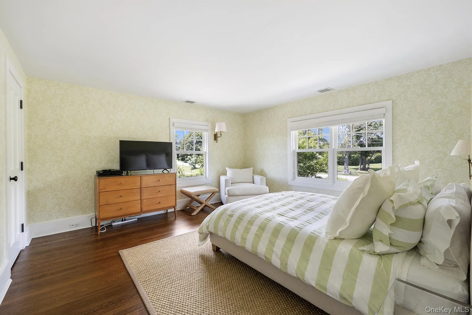 Bedroom with dark wood-type flooring, wallpapered walls, and multiple windows Bedroom with dark wood-type flooring, wallpapered walls, and multiple windows