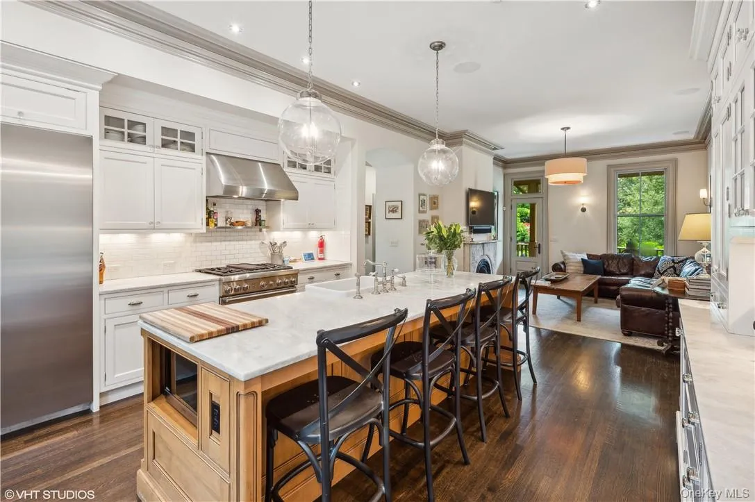 Kitchen with dark wood-type flooring, a kitchen island with sink, wall chimney exhaust hood, appliances with stainless steel finishes, and a kitchen breakfast bar Kitchen with dark wood-type flooring, a kitchen island with sink, wall chimney exhaust hood, appliances with stainless steel finishes, and a kitchen breakfast bar
