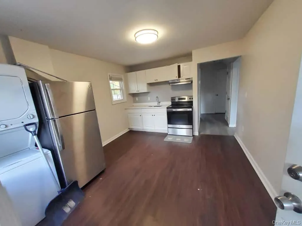 Kitchen with white cabinetry, stainless steel appliances, light countertops, dark wood-style flooring, and under cabinet range hood Kitchen with white cabinetry, stainless steel appliances, light countertops, dark wood-style flooring, and under cabinet range hood