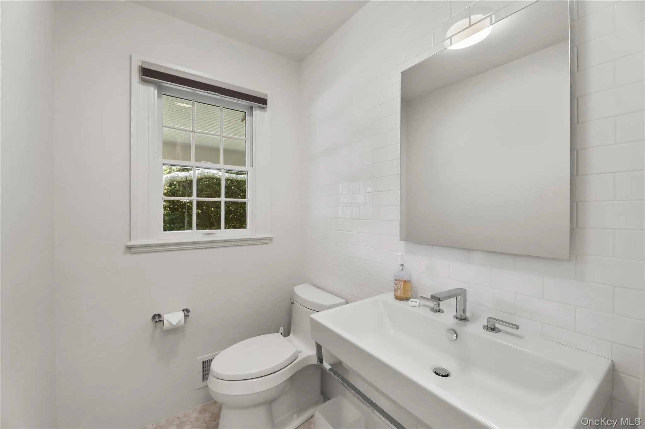 Half bathroom with toilet, visible vents, decorative backsplash, tile walls, and a sink Half bathroom with toilet, visible vents, decorative backsplash, tile walls, and a sink