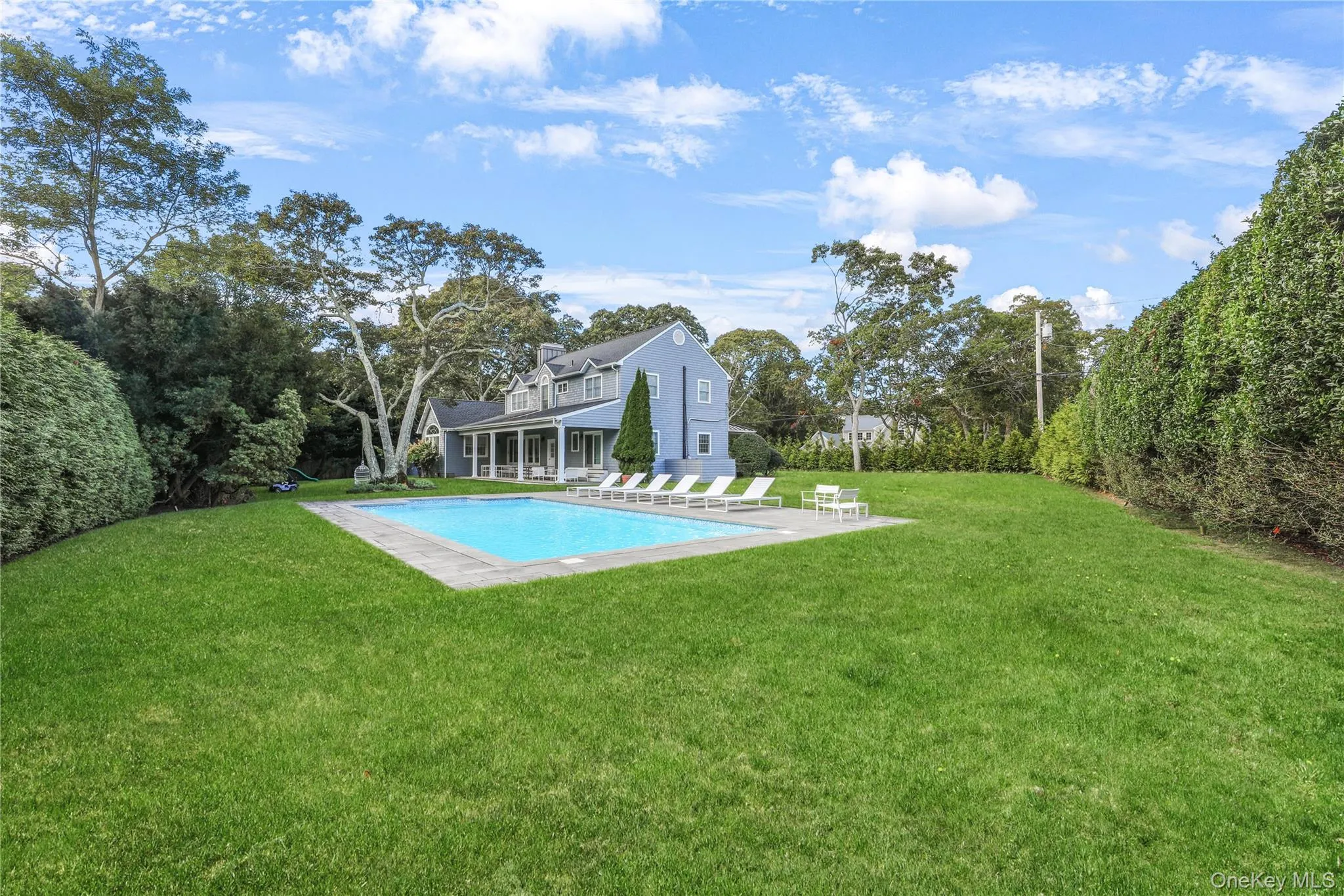 Outdoor pool featuring a patio, a yard, and view of scattered trees Outdoor pool featuring a patio, a yard, and view of scattered trees