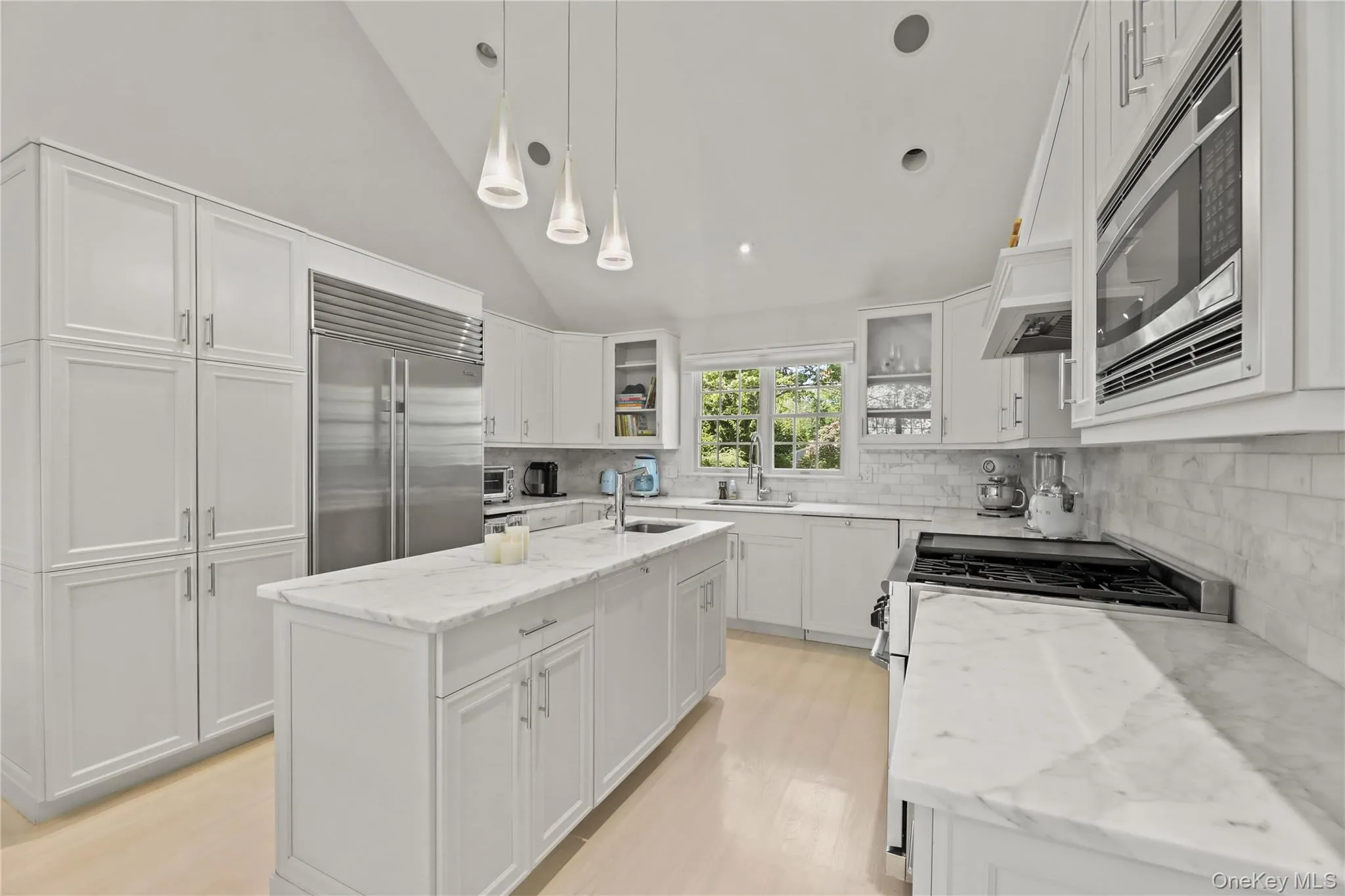 Kitchen with tasteful backsplash, built in appliances, vaulted ceiling, an island with sink, and white cabinets Kitchen with tasteful backsplash, built in appliances, vaulted ceiling, an island with sink, and white cabinets