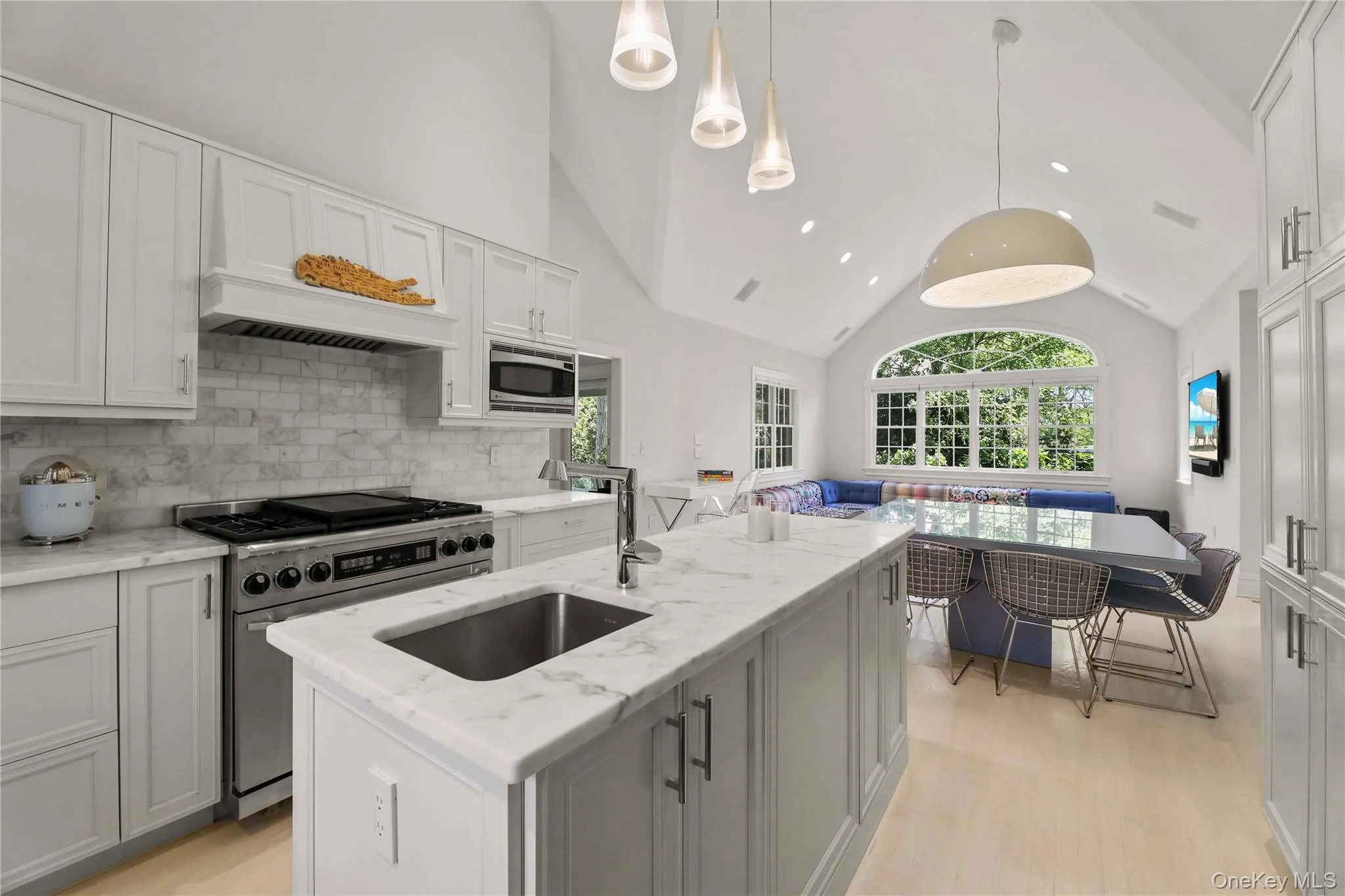 Kitchen featuring light wood-style floors, tasteful backsplash, vaulted ceiling, a sink, and stainless steel appliances Kitchen featuring light wood-style floors, tasteful backsplash, vaulted ceiling, a sink, and stainless steel appliances