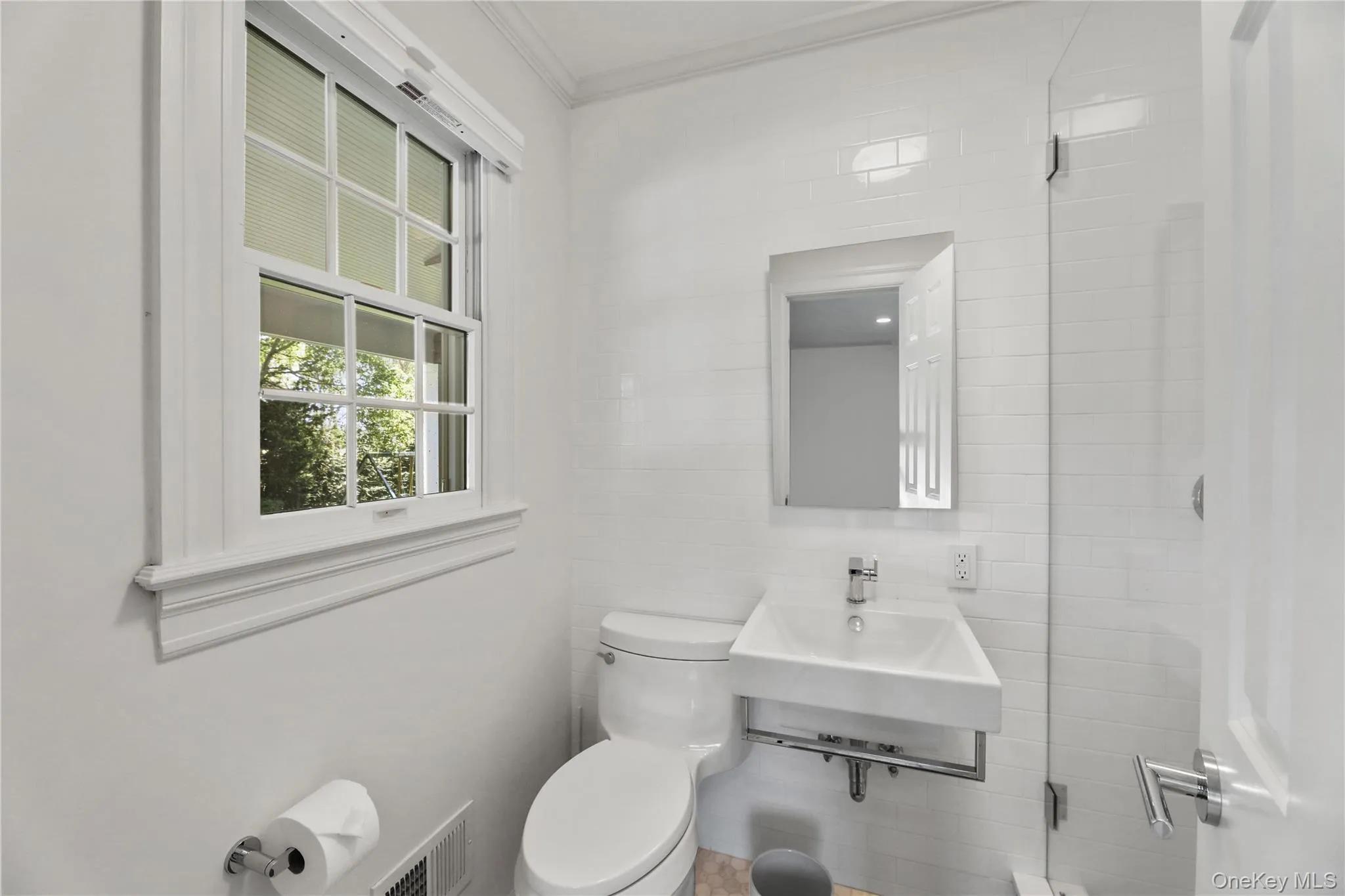 Bathroom with ornamental molding, toilet, visible vents, tile walls, and a sink Bathroom with ornamental molding, toilet, visible vents, tile walls, and a sink