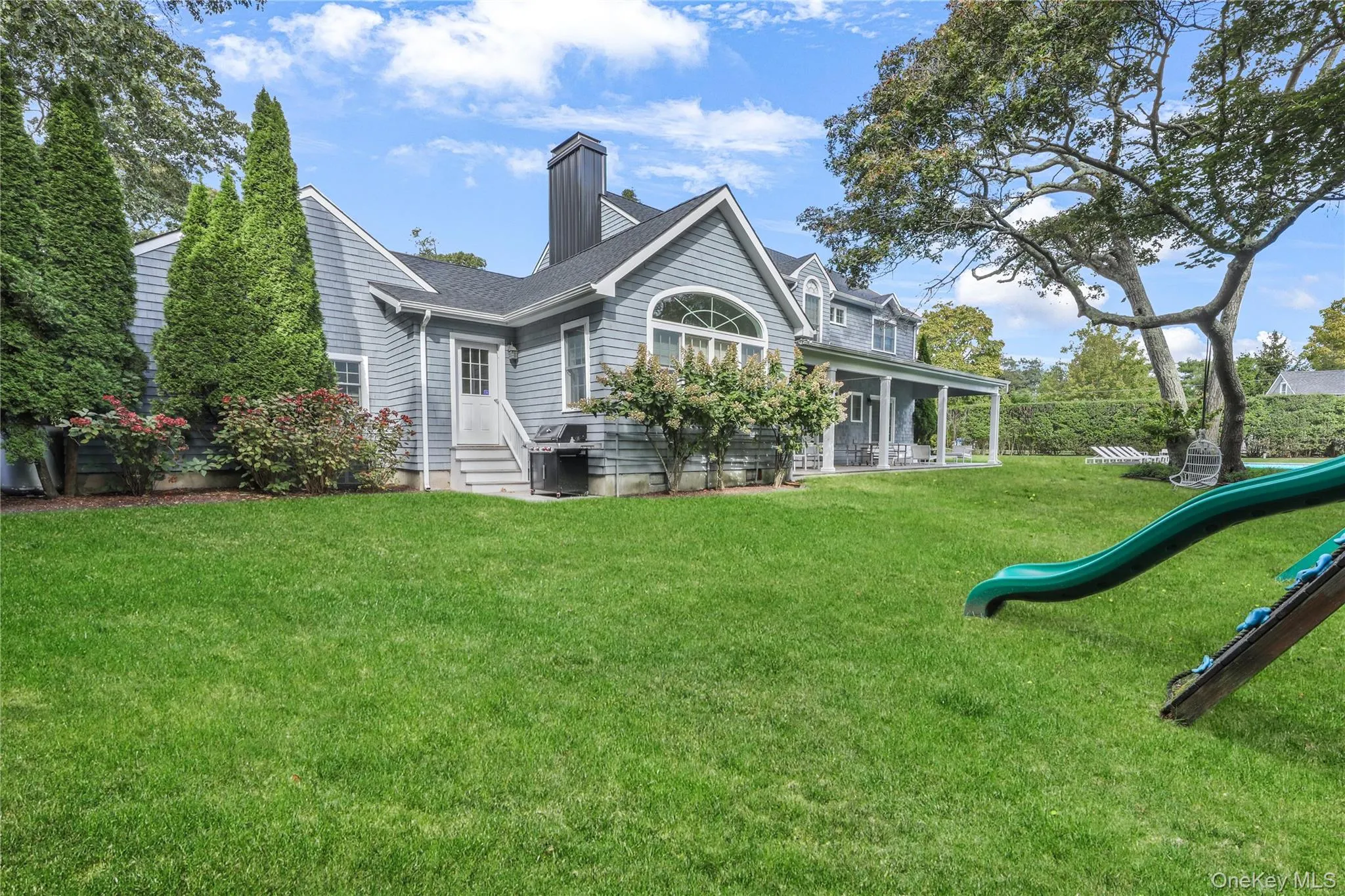 Back of house featuring a chimney, a lawn, a playground, covered porch, and roof with shingles Back of house featuring a chimney, a lawn, a playground, covered porch, and roof with shingles