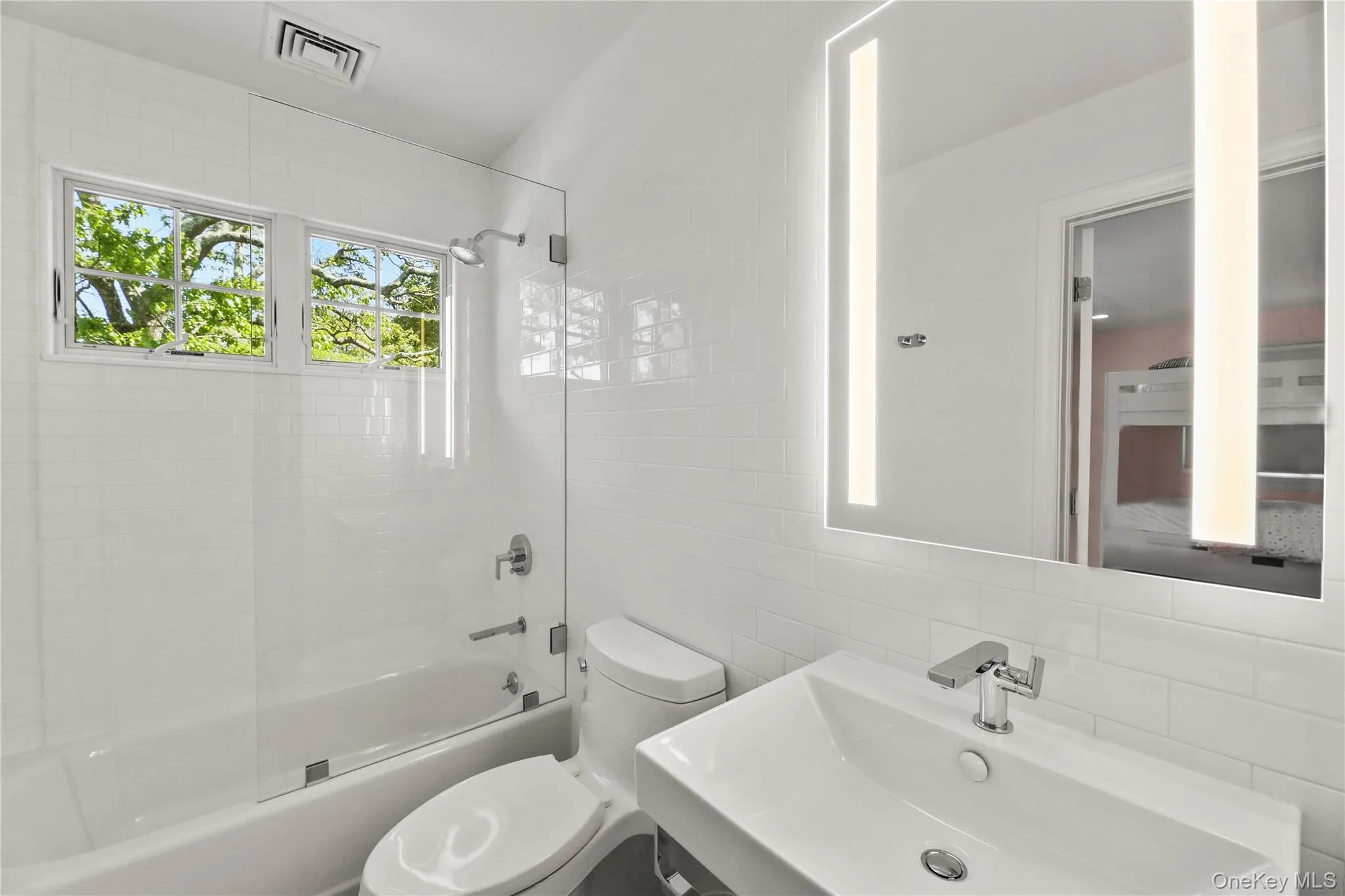 Full bath featuring toilet, visible vents, tile walls, a sink, and tub / shower combination Full bath featuring toilet, visible vents, tile walls, a sink, and tub / shower combination