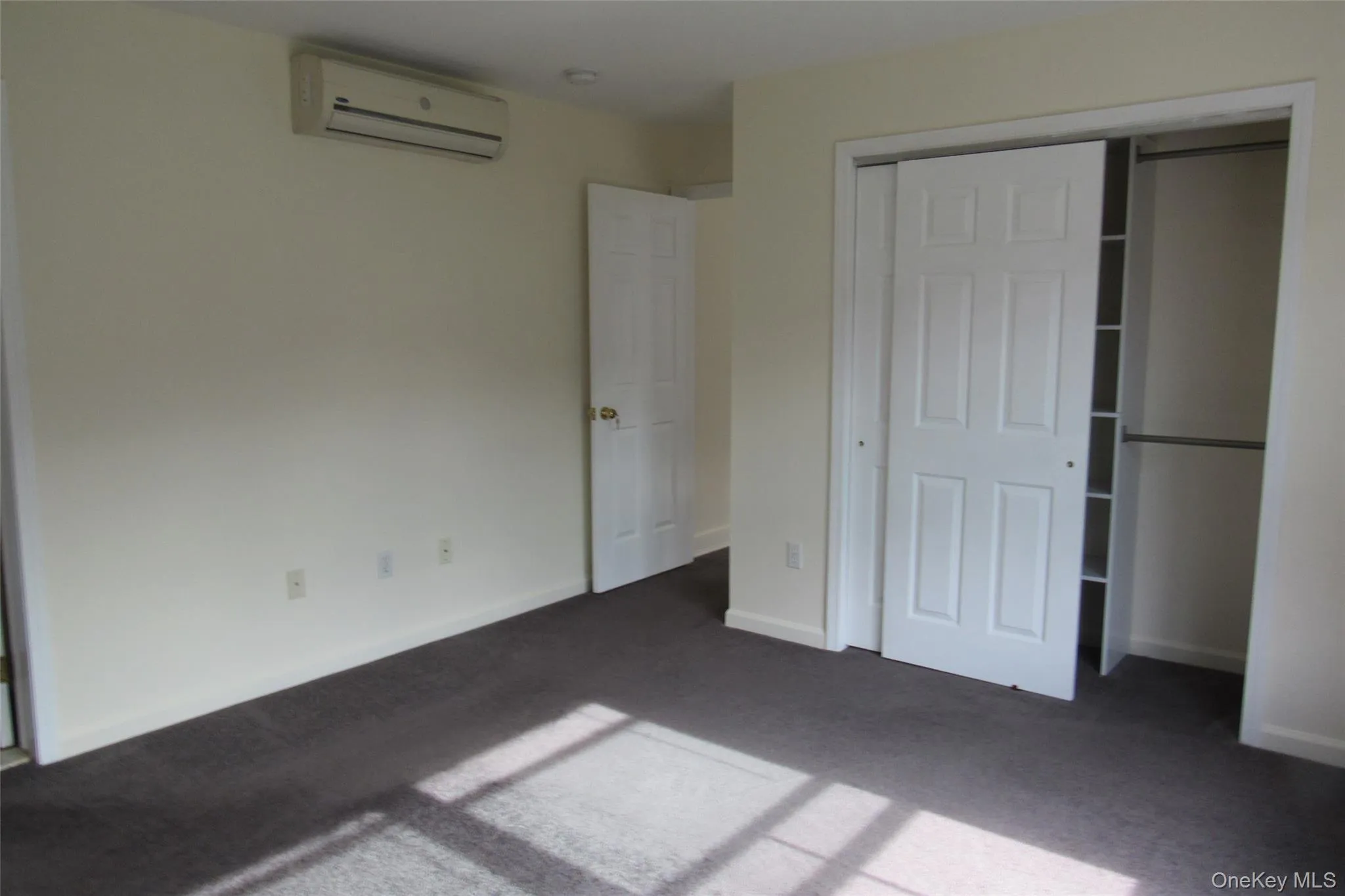 Unfurnished bedroom with a wall unit AC, carpet flooring, and a closet Unfurnished bedroom with a wall unit AC, carpet flooring, and a closet