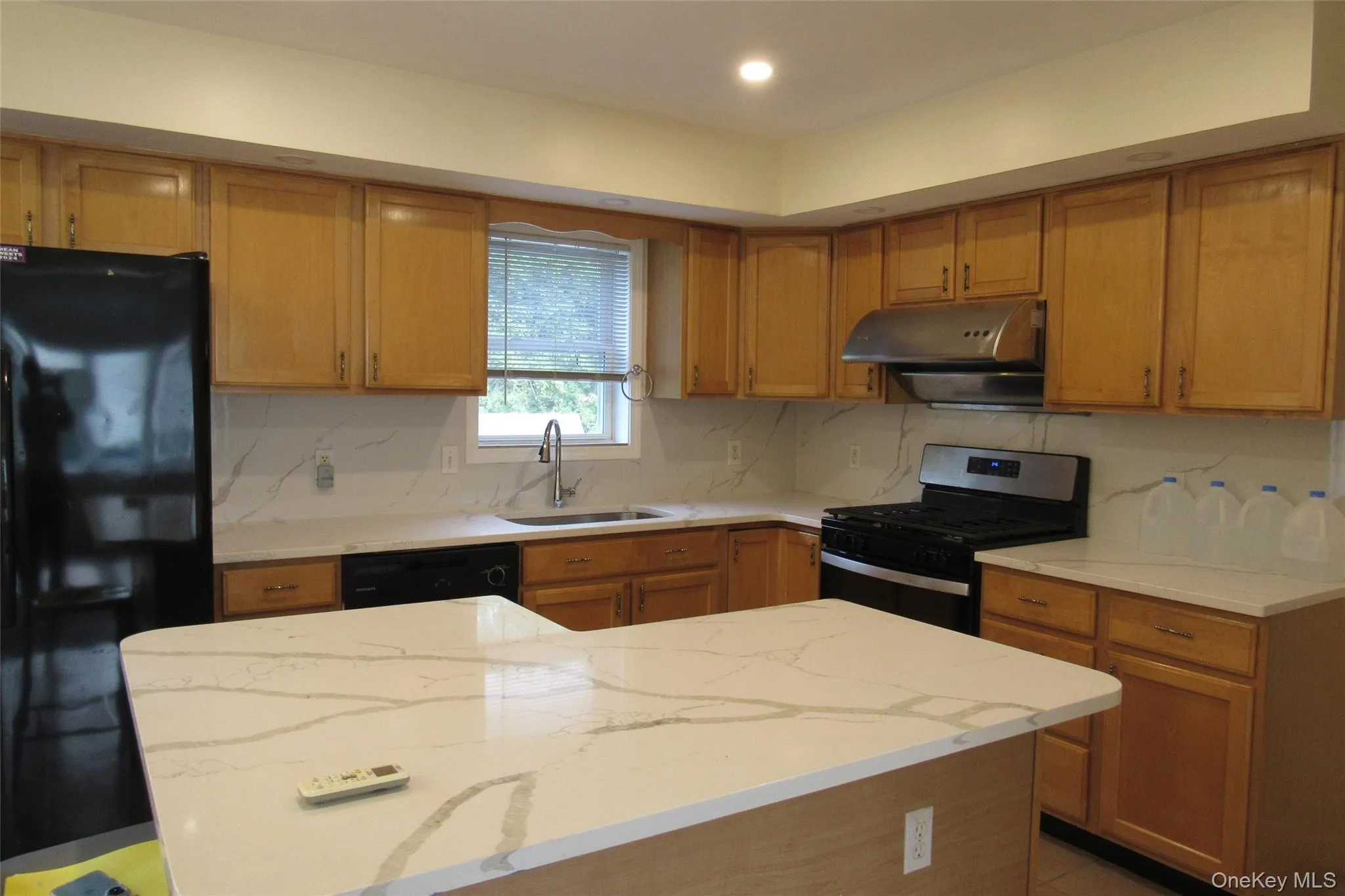 Kitchen with black appliances, light quartz countertops, decorative backsplash, a kitchen island, and brown cabinets Kitchen with black appliances, light quartz countertops, decorative backsplash, a kitchen island, and brown cabinets