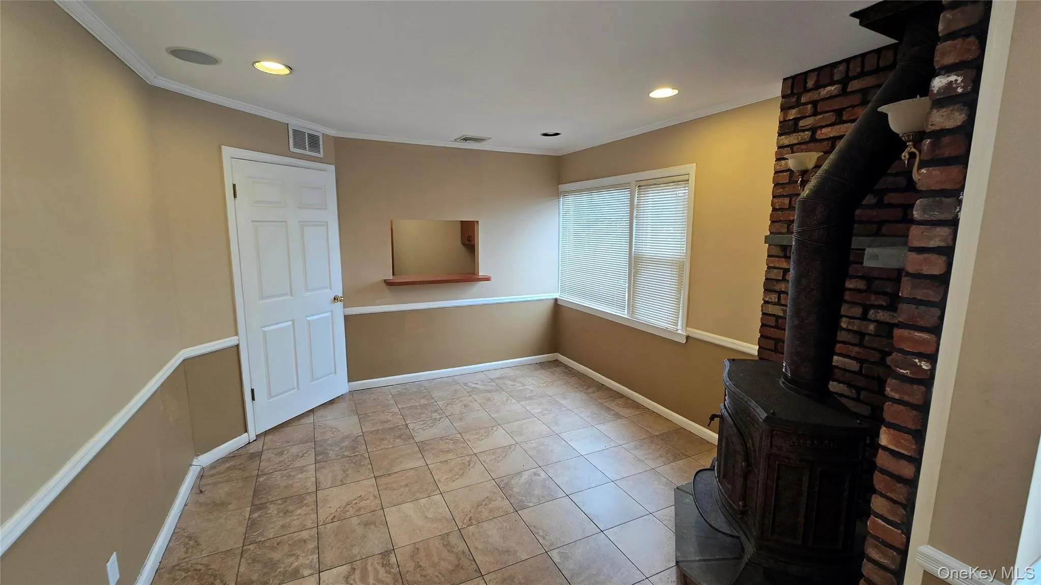 Unfurnished living room featuring a wood stove, crown molding, recessed lighting, and light tile patterned floors Unfurnished living room featuring a wood stove, crown molding, recessed lighting, and light tile patterned floors