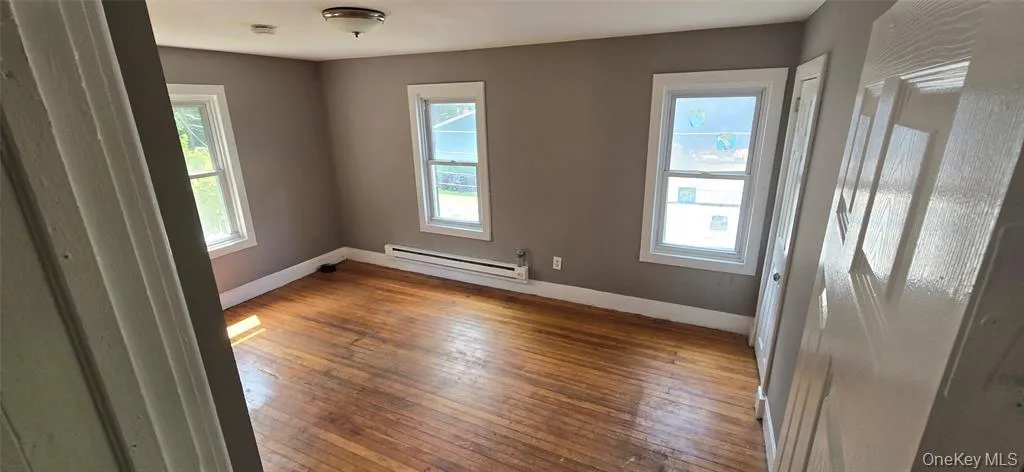 Unfurnished room featuring hardwood / wood-style flooring, baseboards, and baseboard heating Unfurnished room featuring hardwood / wood-style flooring, baseboards, and baseboard heating