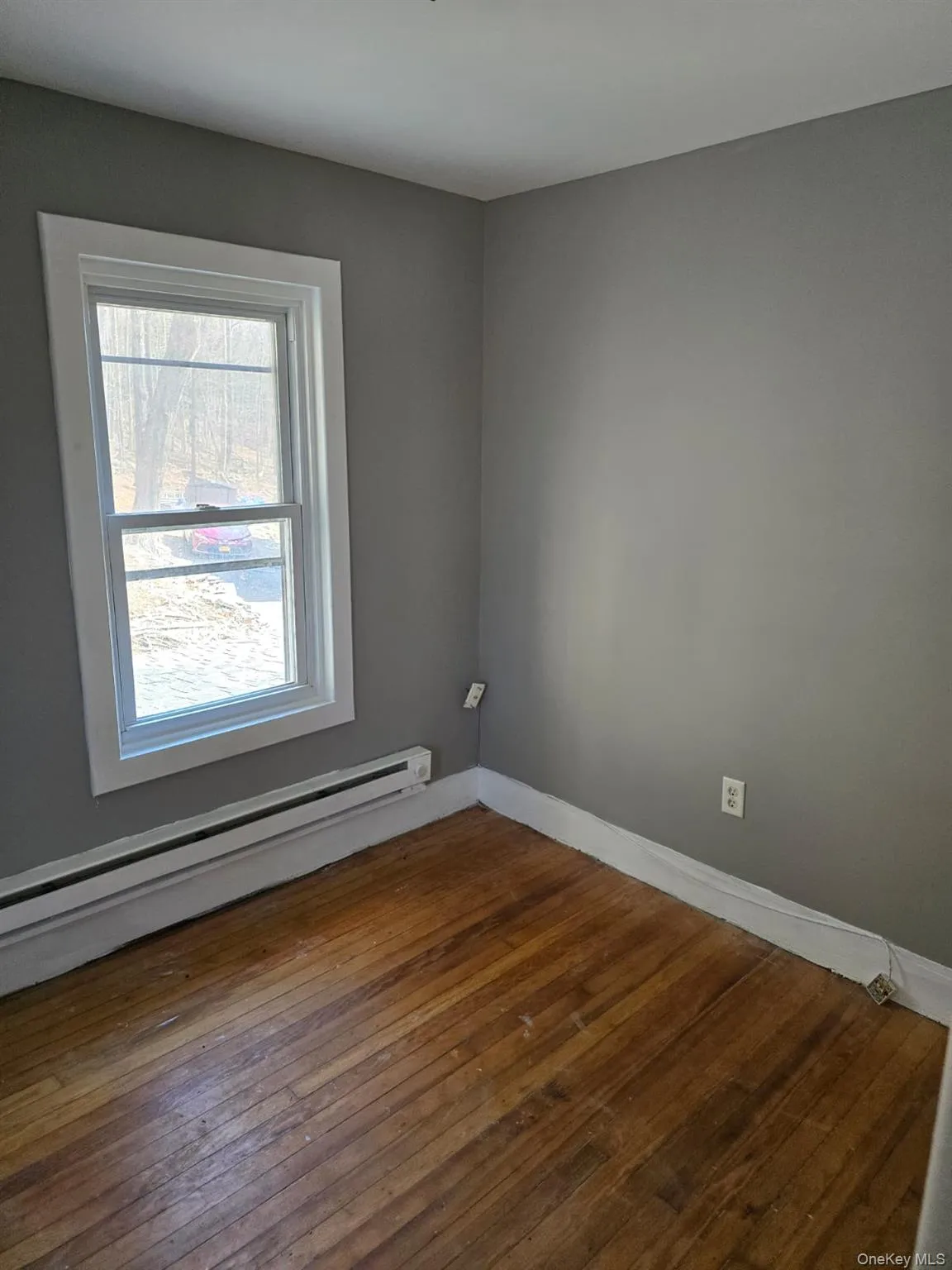 Empty room featuring a baseboard heating unit, baseboards, and dark wood-style floors Empty room featuring a baseboard heating unit, baseboards, and dark wood-style floors