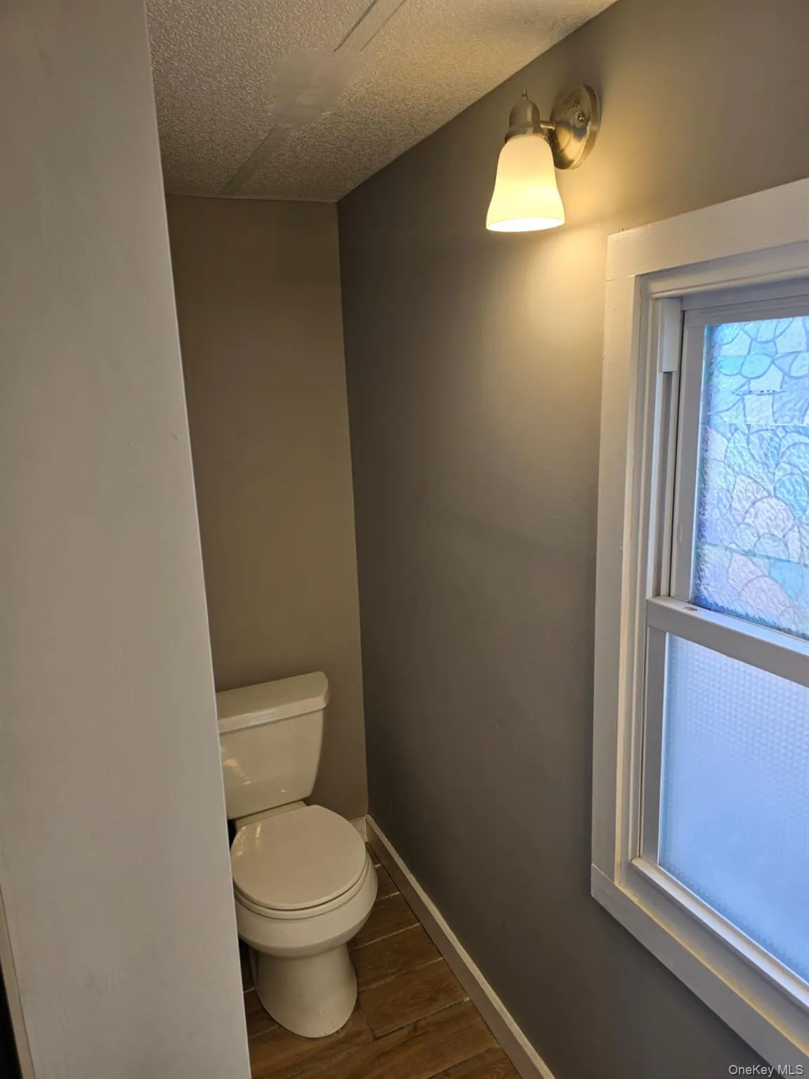 Bathroom with toilet, wood finished floors, baseboards, and a textured ceiling Bathroom with toilet, wood finished floors, baseboards, and a textured ceiling