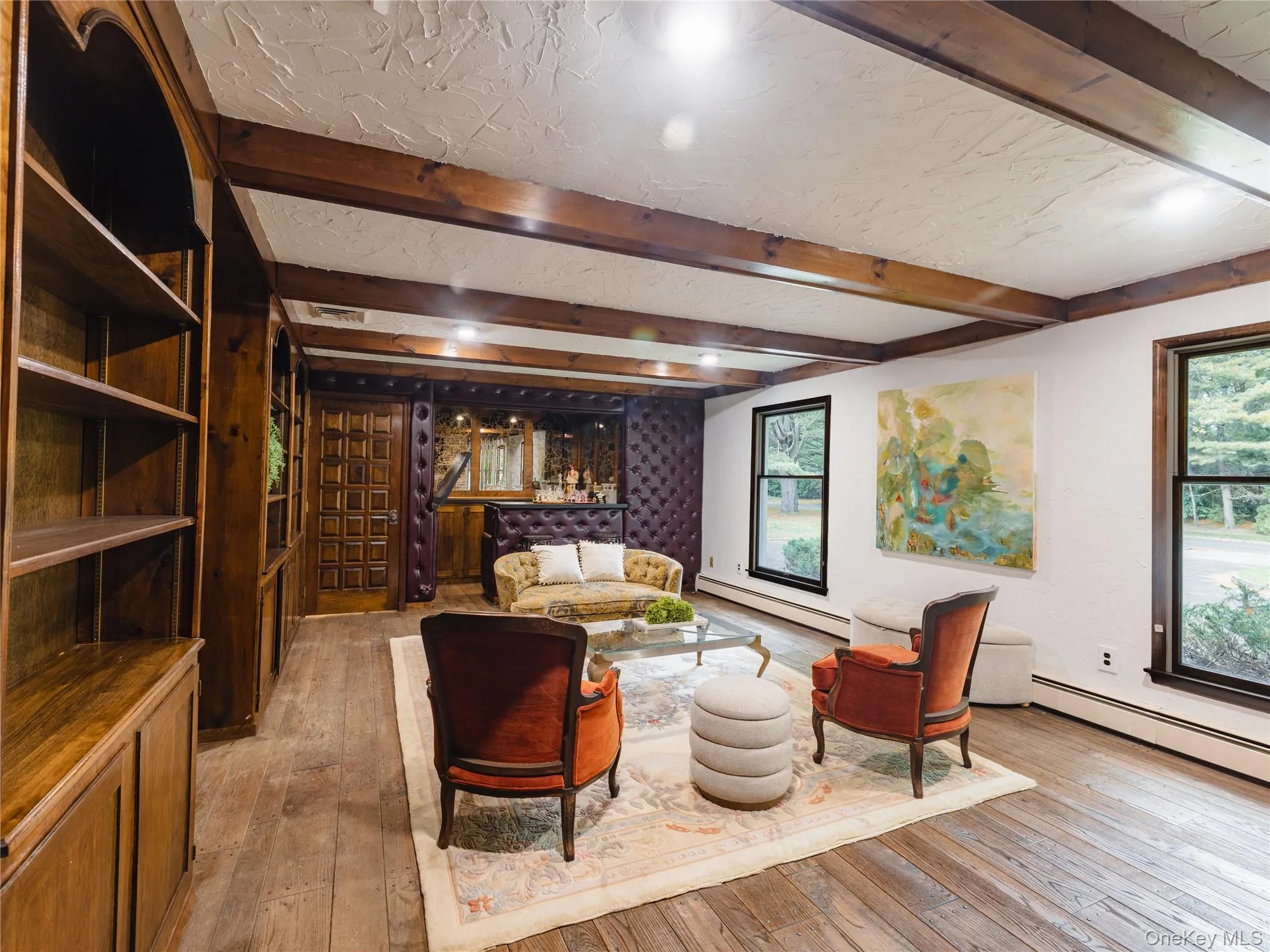 Living area featuring light wood-style flooring, healthy amount of natural light, baseboard heating, and beam ceiling Living area featuring light wood-style flooring, healthy amount of natural light, baseboard heating, and beam ceiling
