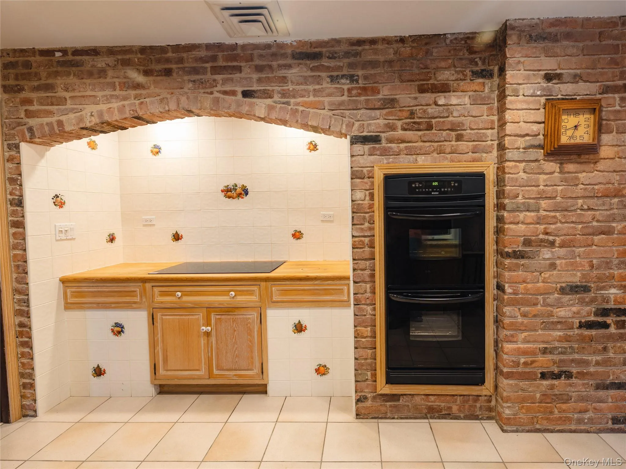 Kitchen featuring black appliances, light tile patterned floors, light countertops, and brick wall Kitchen featuring black appliances, light tile patterned floors, light countertops, and brick wall