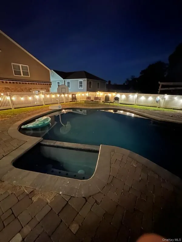 Pool at night with a patio and a pool with connected hot tub Pool at night with a patio and a pool with connected hot tub