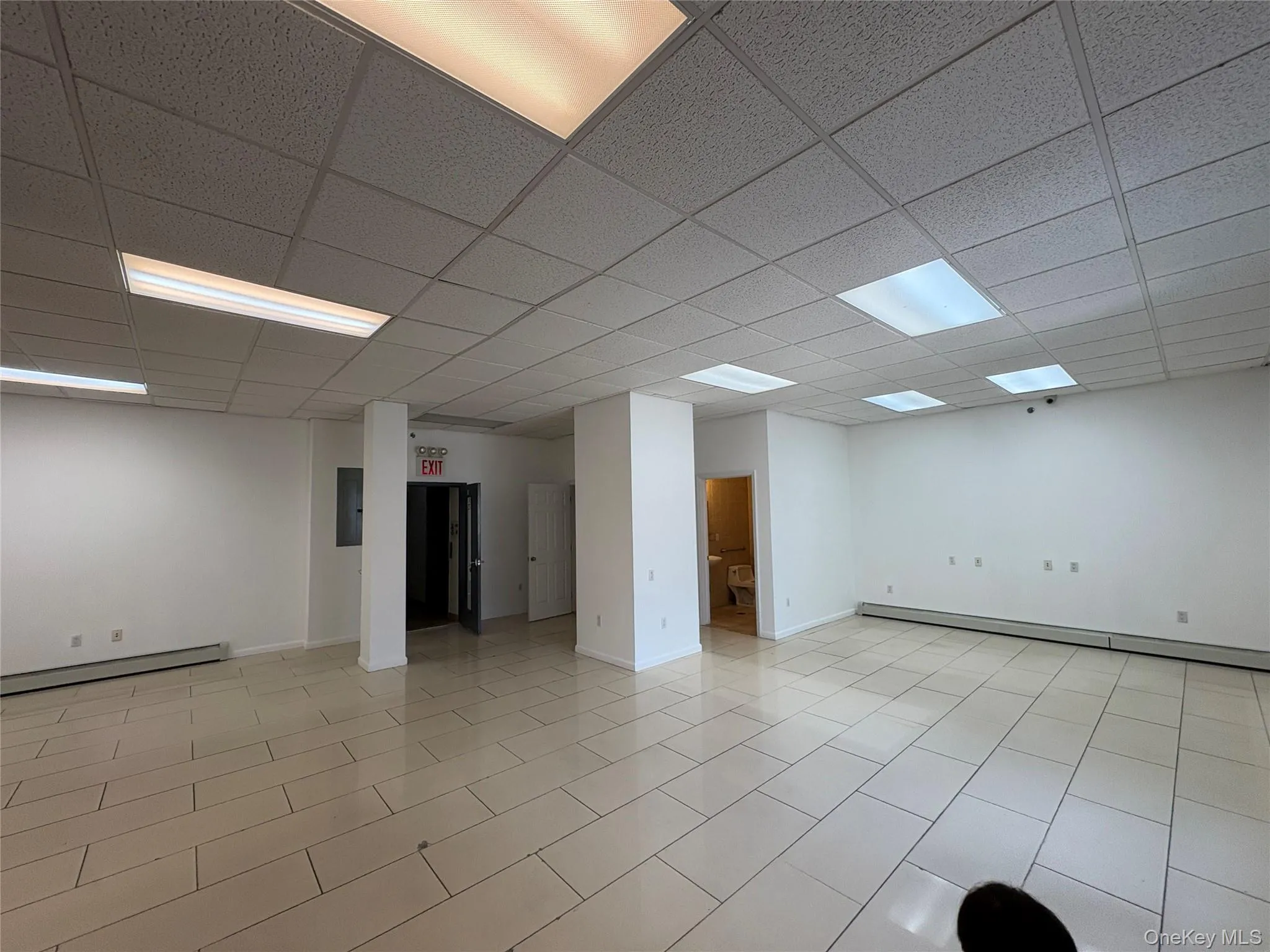 Empty room with a drop ceiling, a baseboard radiator, light tile patterned flooring, and electric panel Empty room with a drop ceiling, a baseboard radiator, light tile patterned flooring, and electric panel