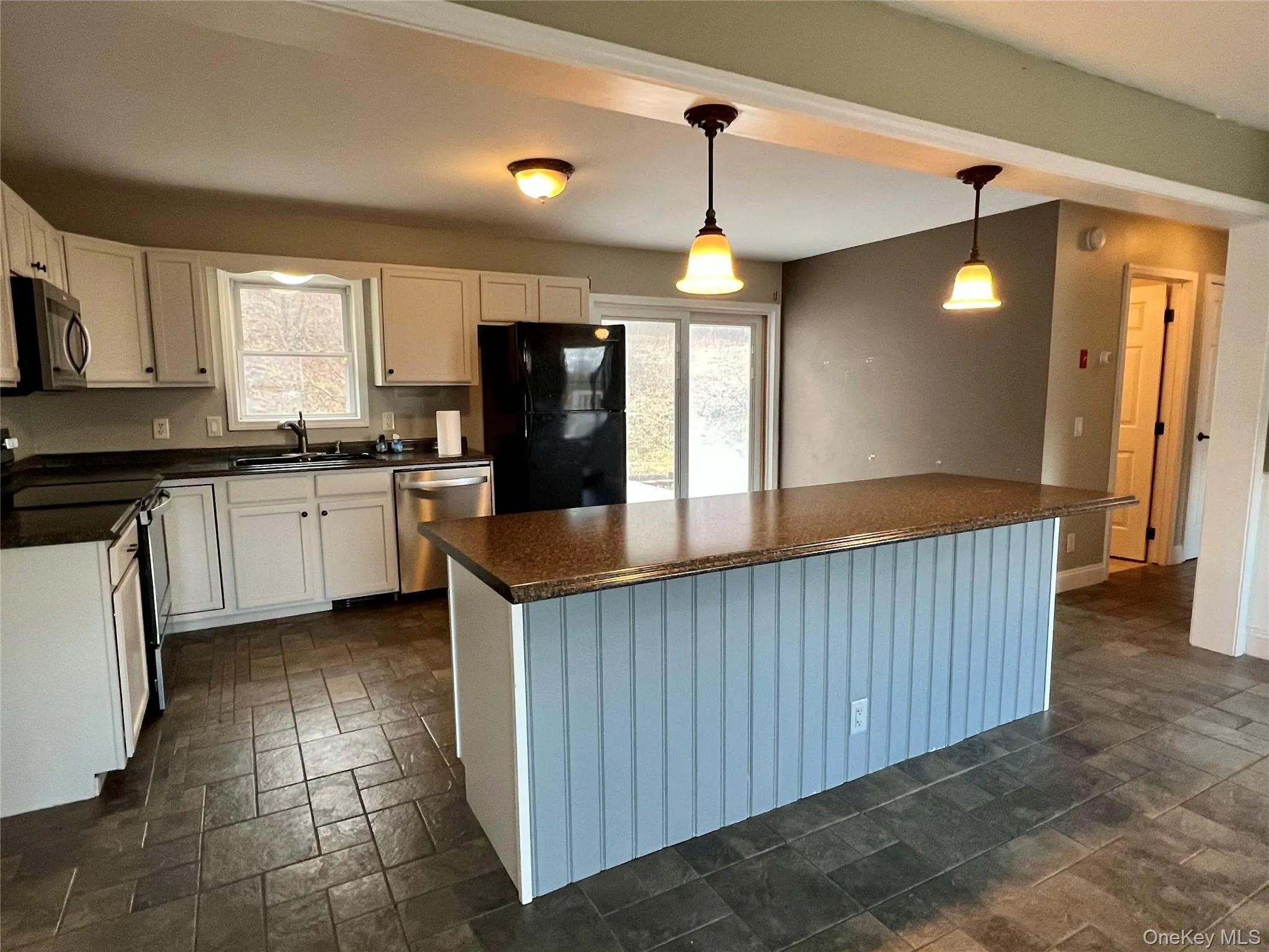 Kitchen featuring stainless steel appliances, pendant lighting, stone tile floors, white cabinetry, and a center island Kitchen featuring stainless steel appliances, pendant lighting, stone tile floors, white cabinetry, and a center island