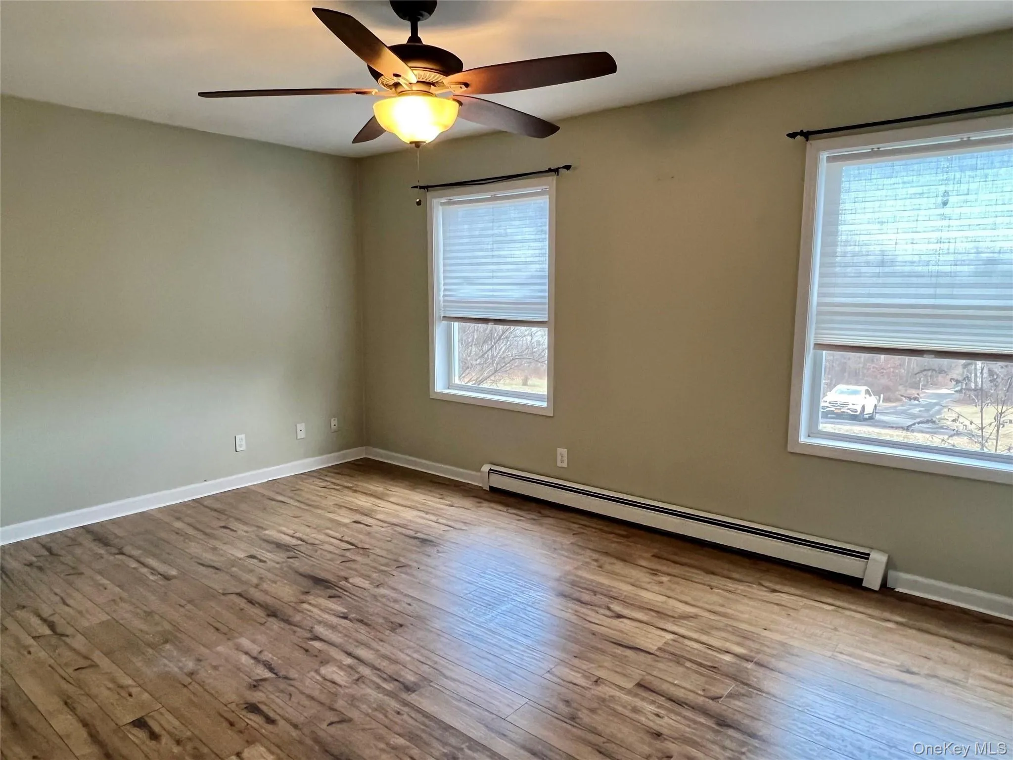 Empty room featuring baseboard heating, hardwood / wood-style flooring, and plenty of natural light Empty room featuring baseboard heating, hardwood / wood-style flooring, and plenty of natural light