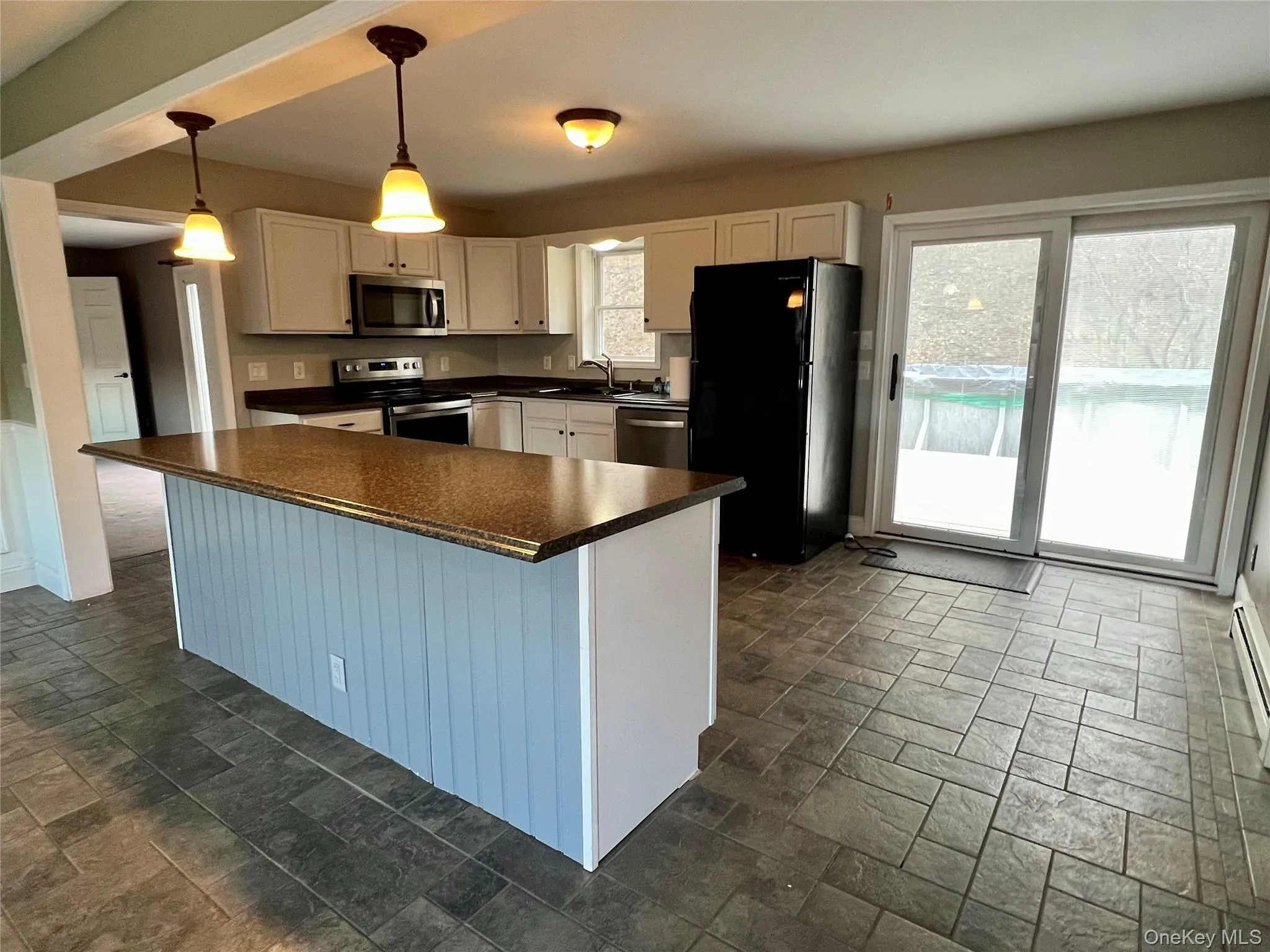 Kitchen featuring dark countertops, stainless steel appliances, dark stone finish floors, pendant lighting, and a center island Kitchen featuring dark countertops, stainless steel appliances, dark stone finish floors, pendant lighting, and a center island