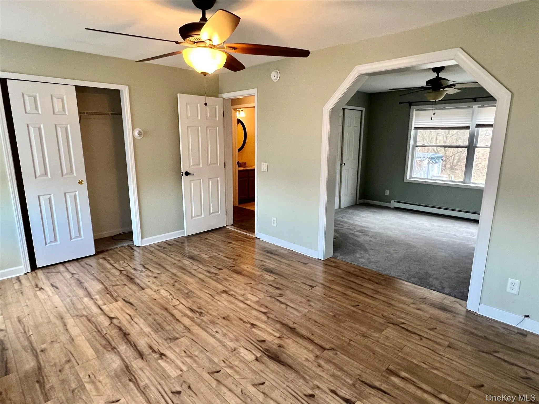 Unfurnished bedroom featuring a baseboard heating unit, light wood-type flooring, ceiling fan, arched walkways, and a closet Unfurnished bedroom featuring a baseboard heating unit, light wood-type flooring, ceiling fan, arched walkways, and a closet