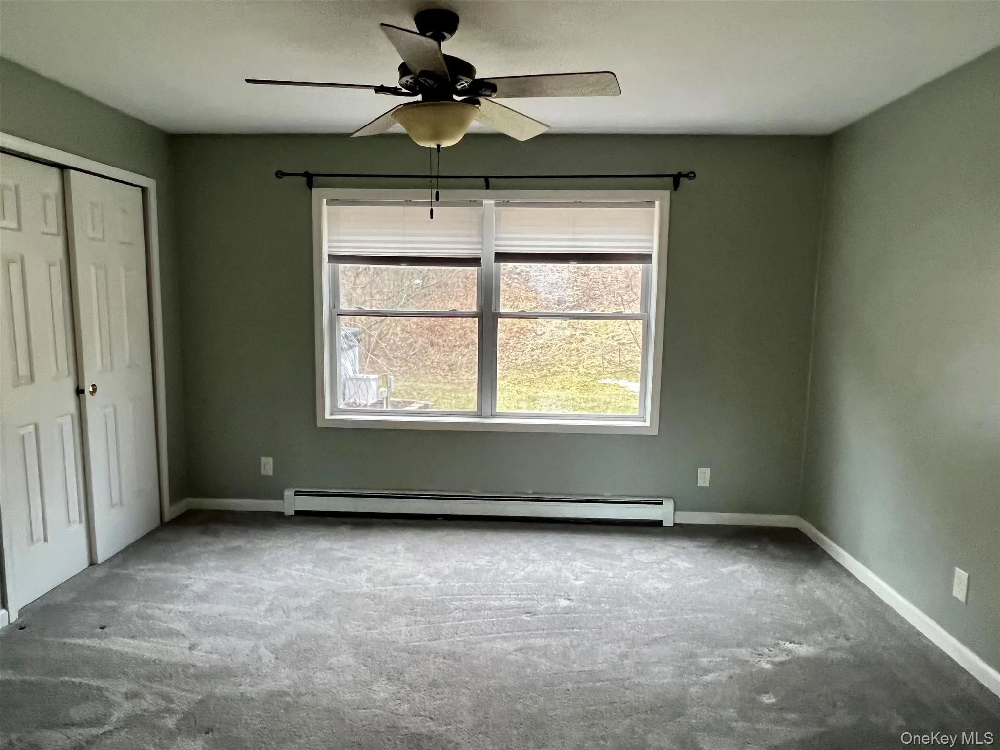Carpeted space room featuren bedroom featuring carpet, baseboard heating, a closet, and a ceiling fan Carpeted space room featuren bedroom featuring carpet, baseboard heating, a closet, and a ceiling fan