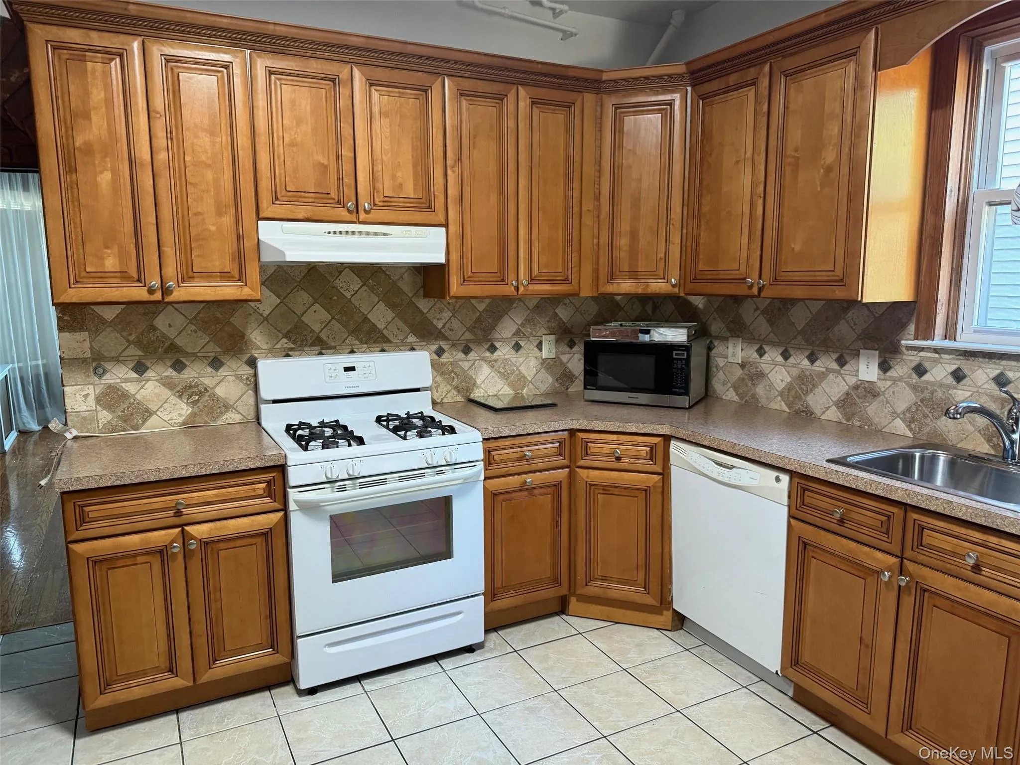 Kitchen with brown cabinets, white appliances, and under cabinet range hood Kitchen with brown cabinets, white appliances, and under cabinet range hood