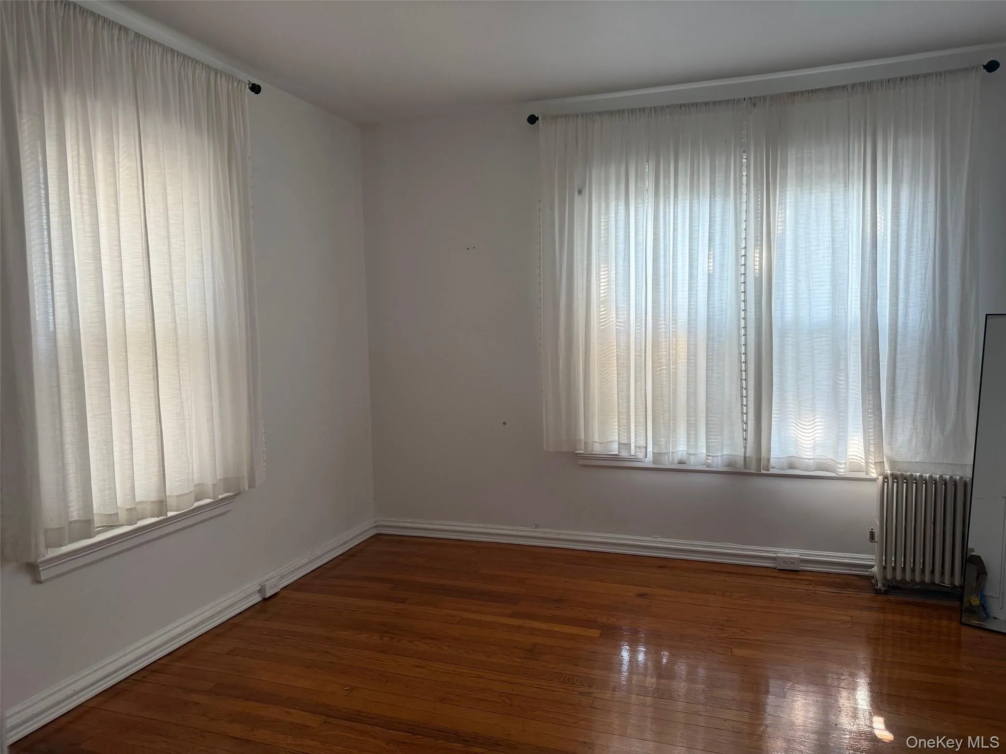 Empty room featuring dark wood-type flooring and radiator heating unit Empty room featuring dark wood-type flooring and radiator heating unit