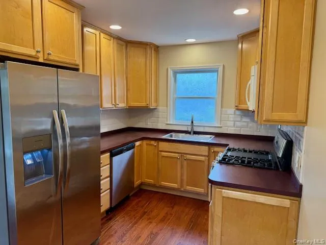 Kitchen with dark countertops, appliances with stainless steel finishes, dark wood-style flooring, tasteful backsplash, and recessed lighting Kitchen with dark countertops, appliances with stainless steel finishes, dark wood-style flooring, tasteful backsplash, and recessed lighting