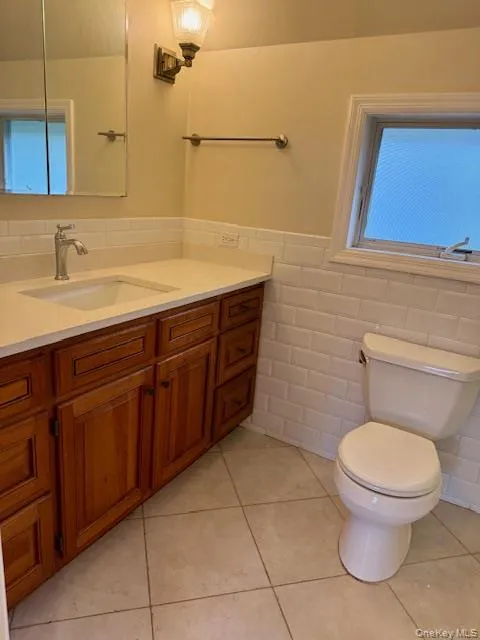 Bathroom with tile walls, vanity, a wainscoted wall, and light tile patterned floors Bathroom with tile walls, vanity, a wainscoted wall, and light tile patterned floors