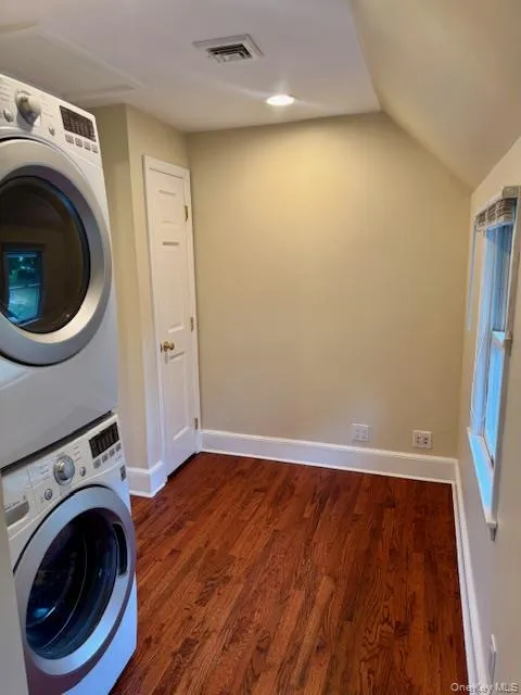 Laundry room with dark wood-style flooring, stacked washer / drying machine, and recessed lighting Laundry room with dark wood-style flooring, stacked washer / drying machine, and recessed lighting