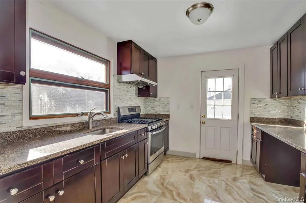 Kitchen featuring stainless steel gas range oven, dark stone countertops, backsplash, and under cabinet range hood Kitchen featuring stainless steel gas range oven, dark stone countertops, backsplash, and under cabinet range hood
