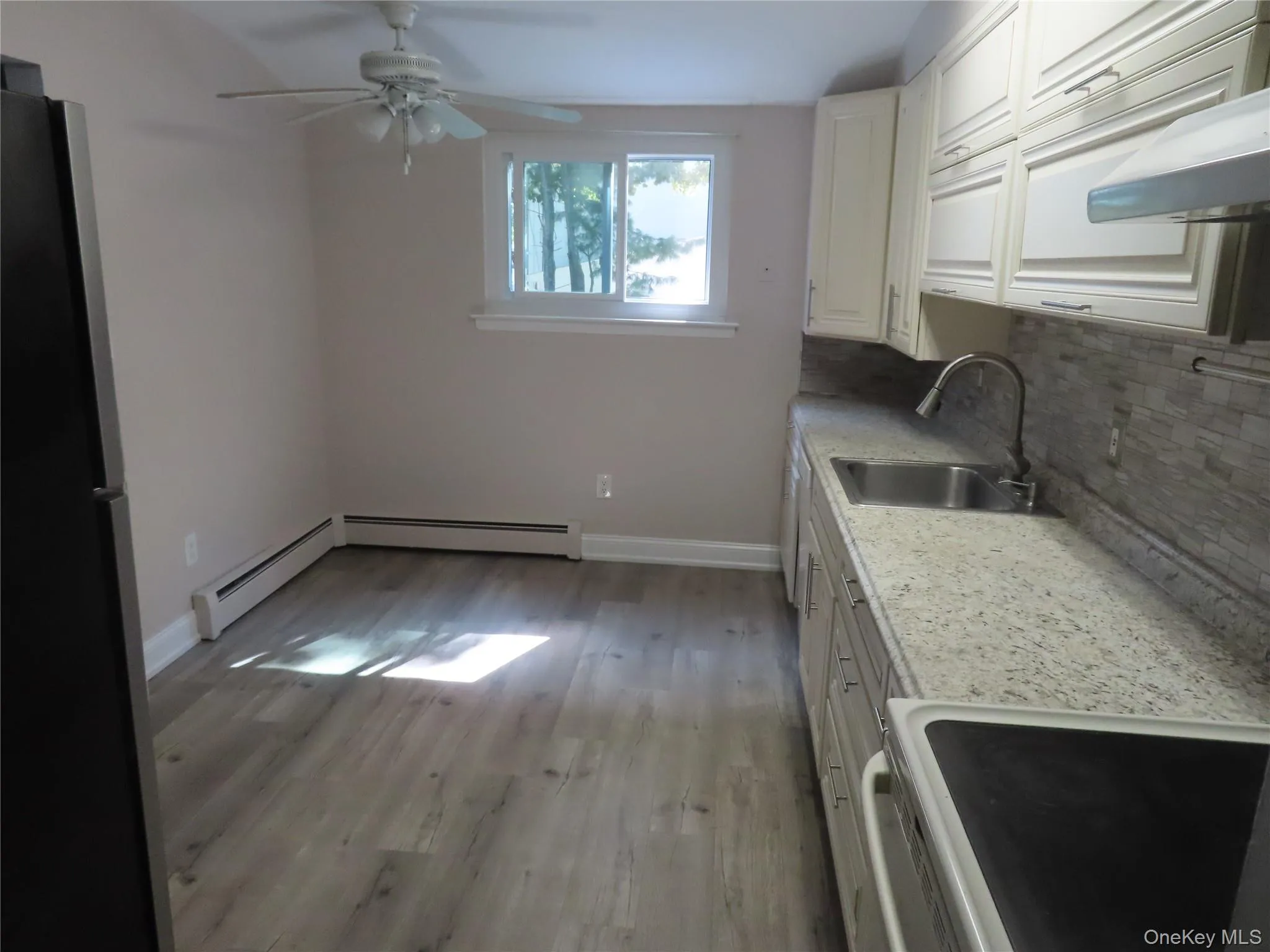 Kitchen featuring stove, backsplash, freestanding refrigerator, white cabinetry, and light wood finished floors Kitchen featuring stove, backsplash, freestanding refrigerator, white cabinetry, and light wood finished floors