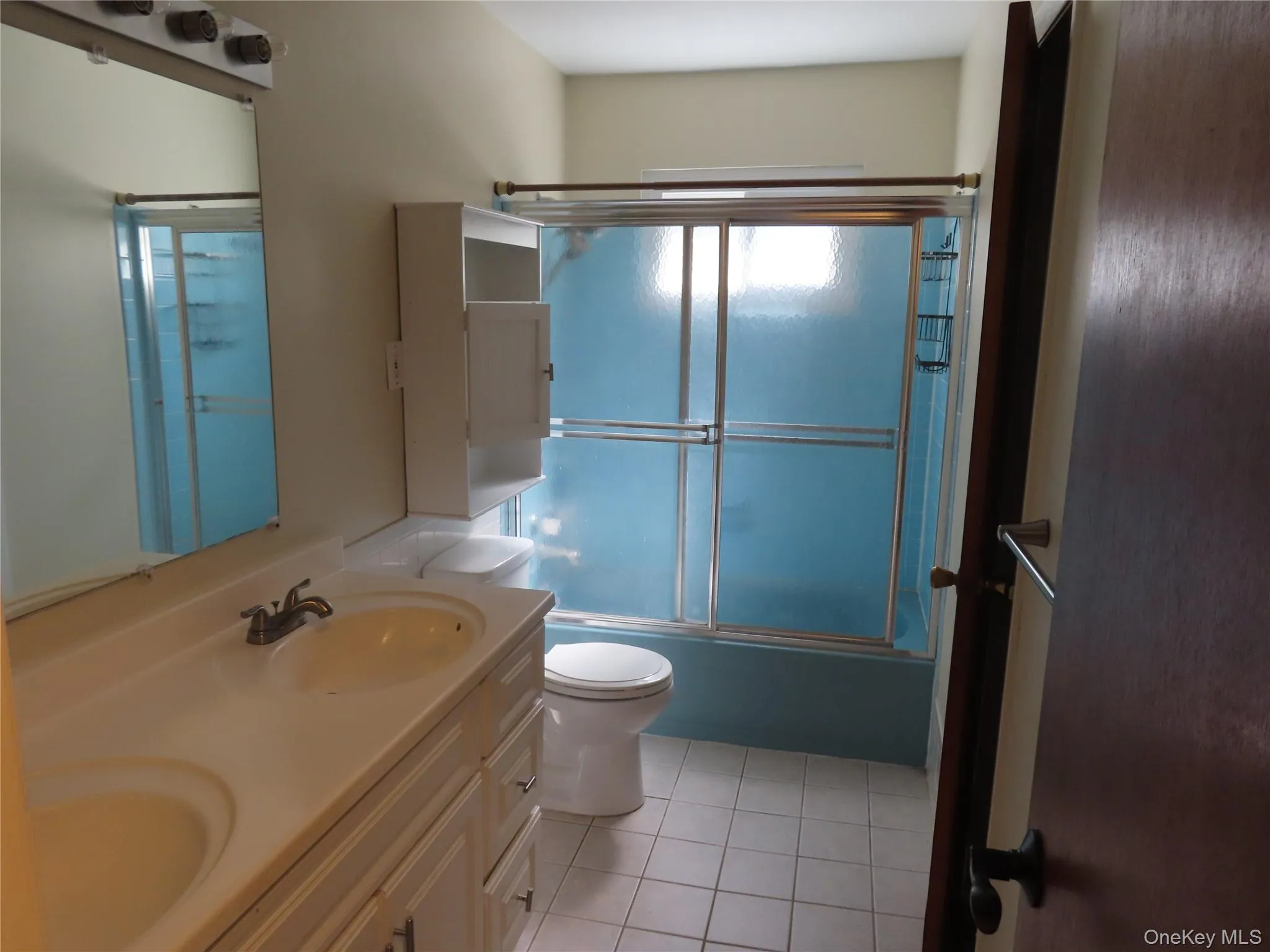 Bathroom featuring enclosed tub / shower combo, light tile patterned floors, and double vanity Bathroom featuring enclosed tub / shower combo, light tile patterned floors, and double vanity