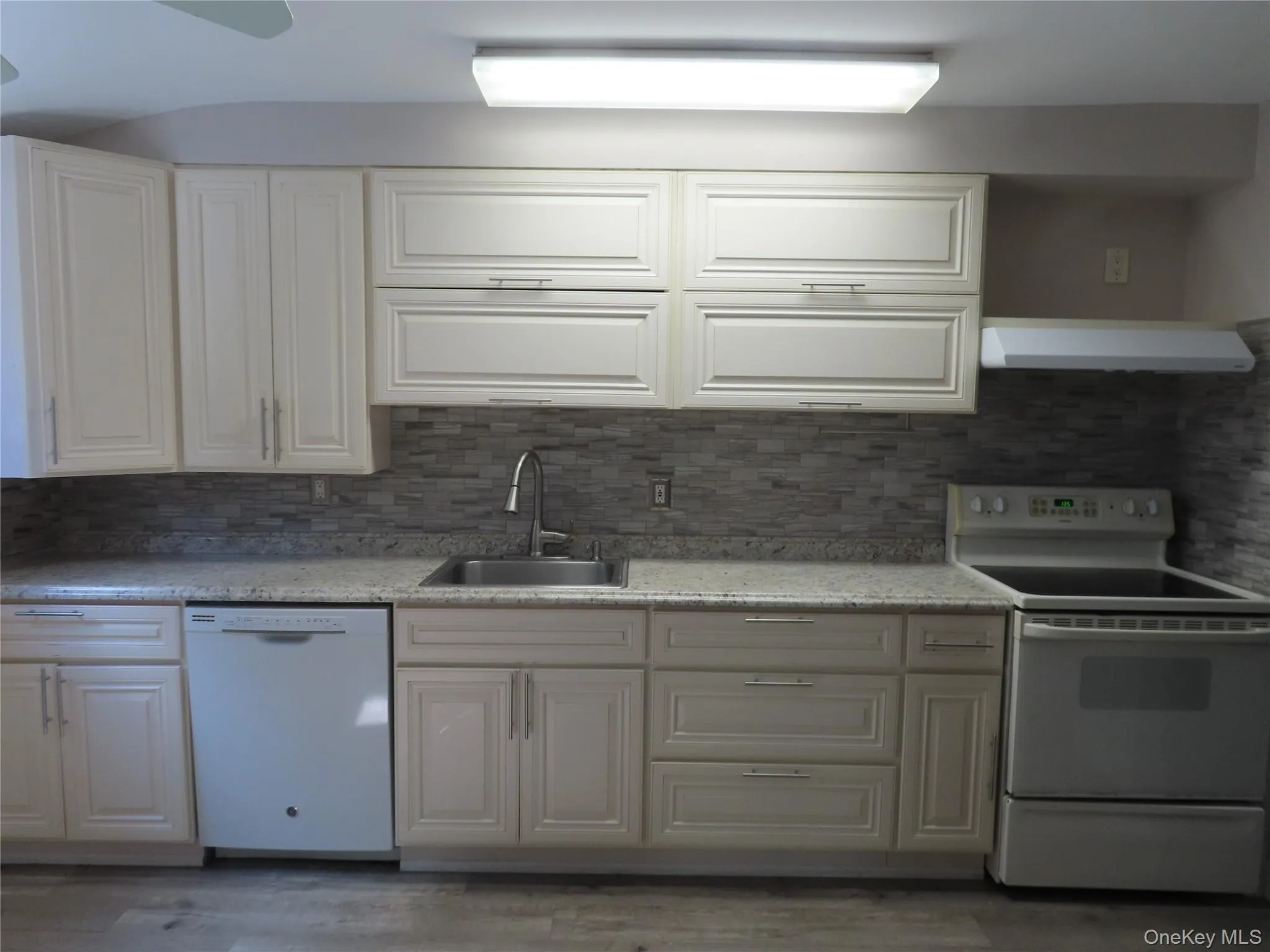 Kitchen featuring white appliances, backsplash, range hood, and white cabinetry Kitchen featuring white appliances, backsplash, range hood, and white cabinetry