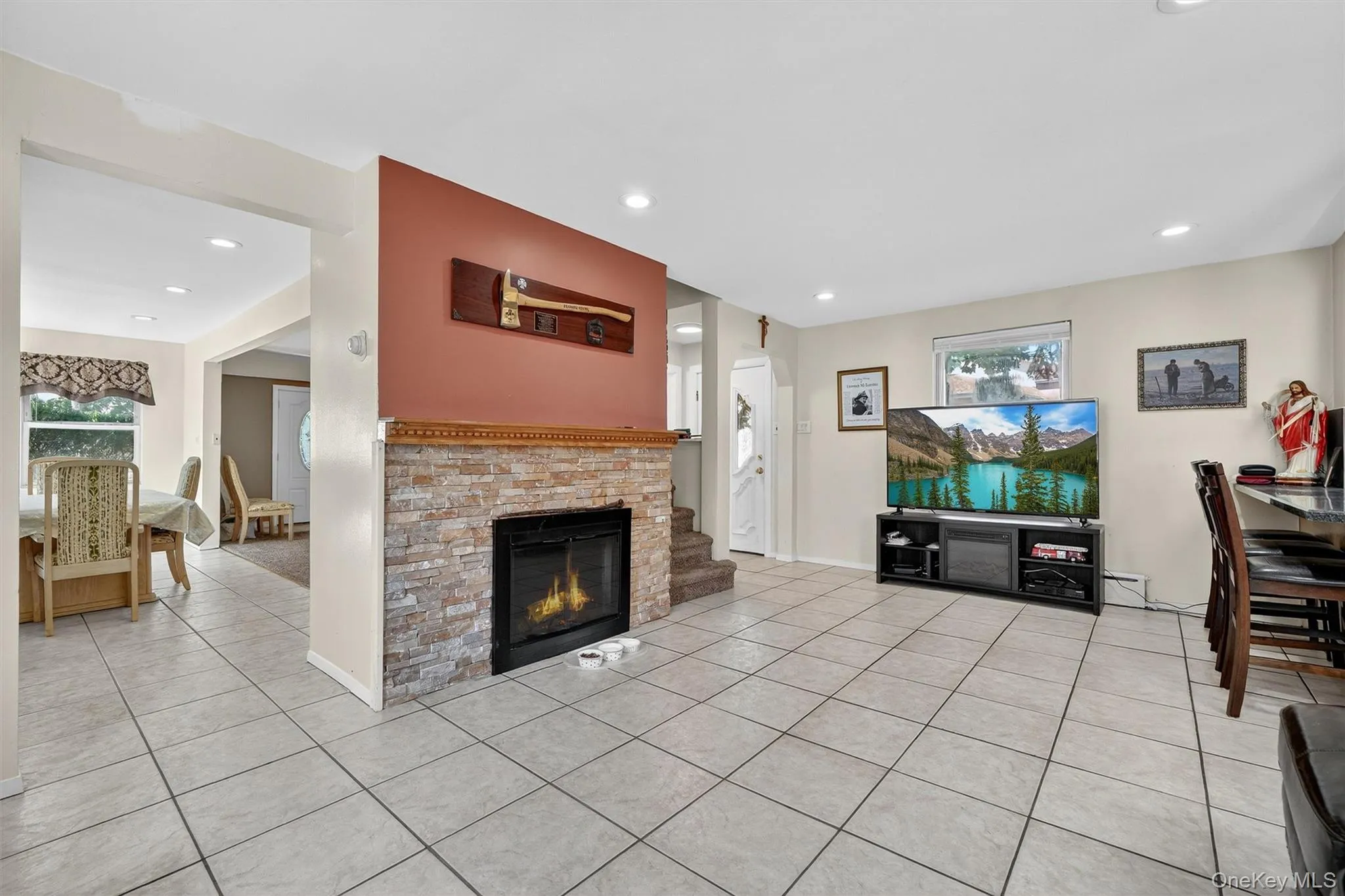 Living room featuring light tile patterned flooring, a glass covered fireplace, recessed lighting, and a baseboard heating unit Living room featuring light tile patterned flooring, a glass covered fireplace, recessed lighting, and a baseboard heating unit
