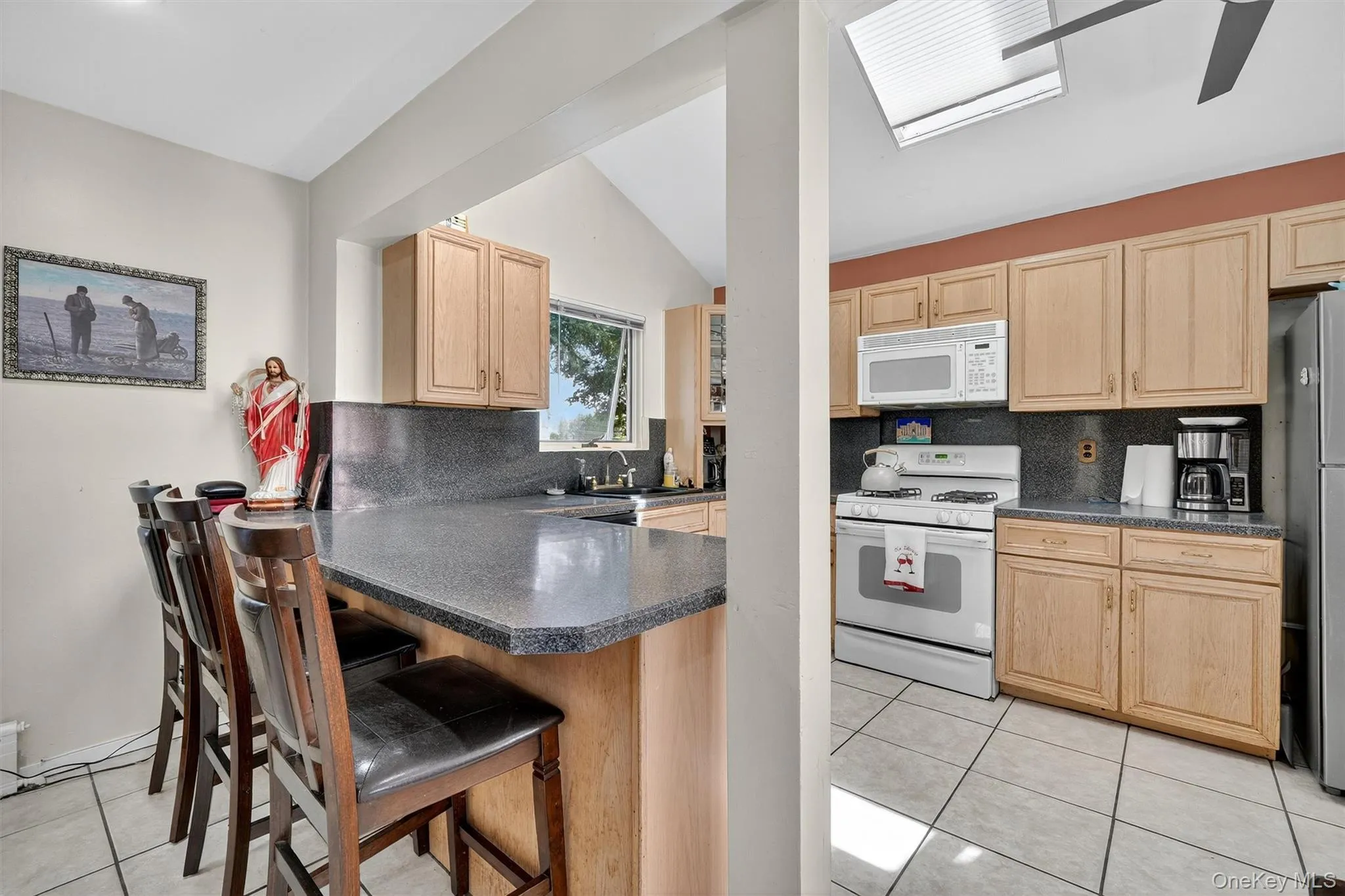 Kitchen with light brown cabinets, light tile patterned flooring, white appliances, decorative backsplash, and lofted ceiling Kitchen with light brown cabinets, light tile patterned flooring, white appliances, decorative backsplash, and lofted ceiling