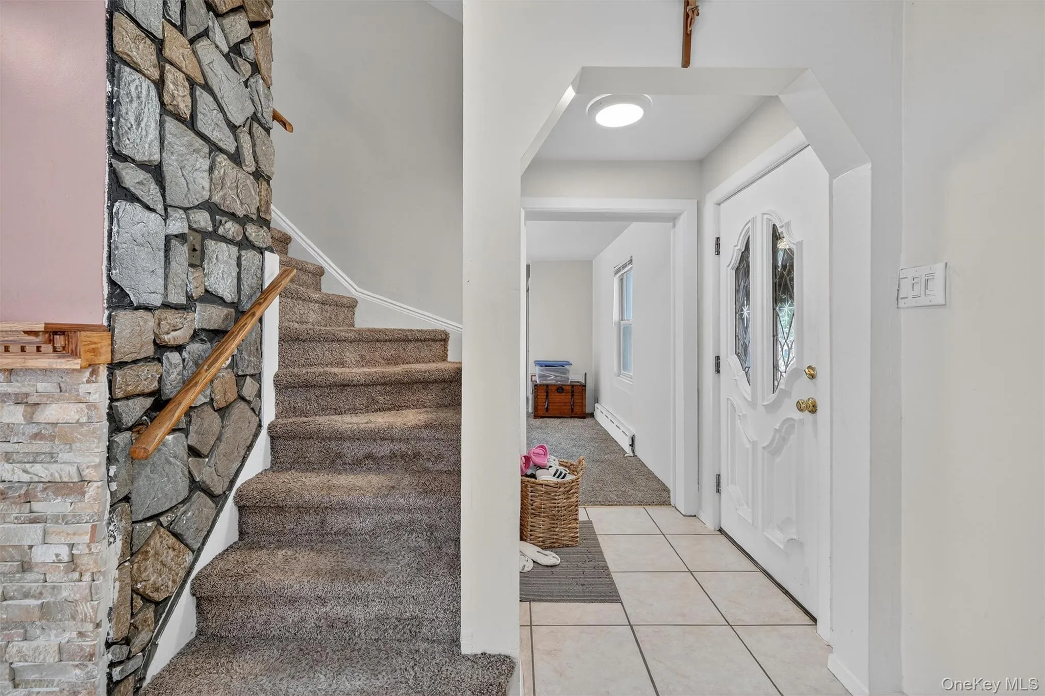 Foyer entrance featuring light tile patterned floors, light colored carpet, a baseboard heating unit, stairs, and arched walkways Foyer entrance featuring light tile patterned floors, light colored carpet, a baseboard heating unit, stairs, and arched walkways