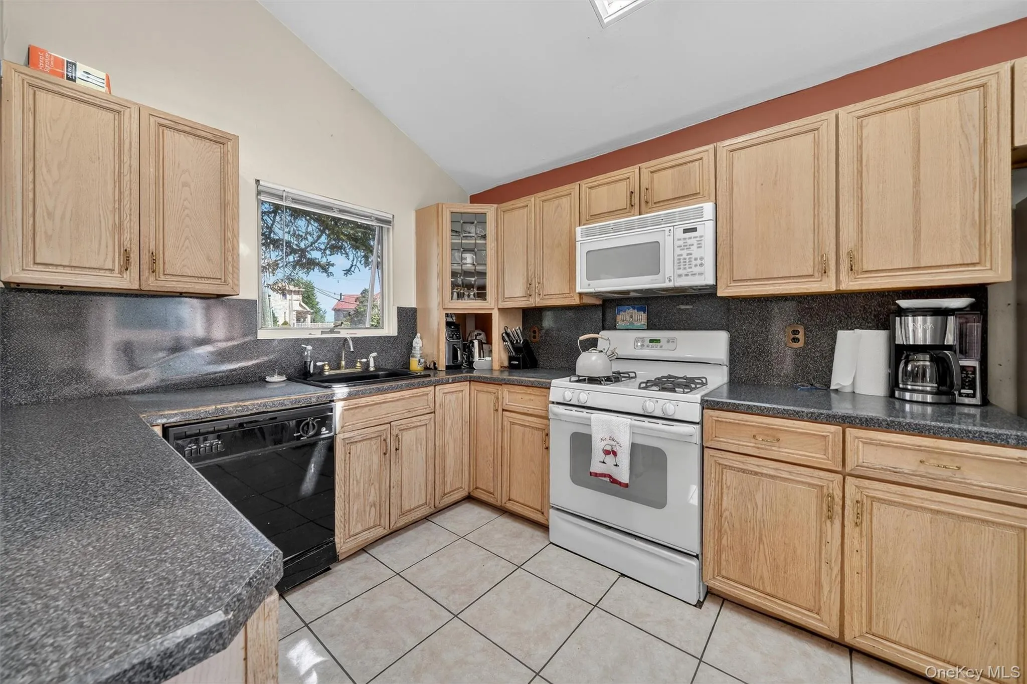 Kitchen with light brown cabinetry, white appliances, vaulted ceiling, tasteful backsplash, and light tile patterned floors Kitchen with light brown cabinetry, white appliances, vaulted ceiling, tasteful backsplash, and light tile patterned floors