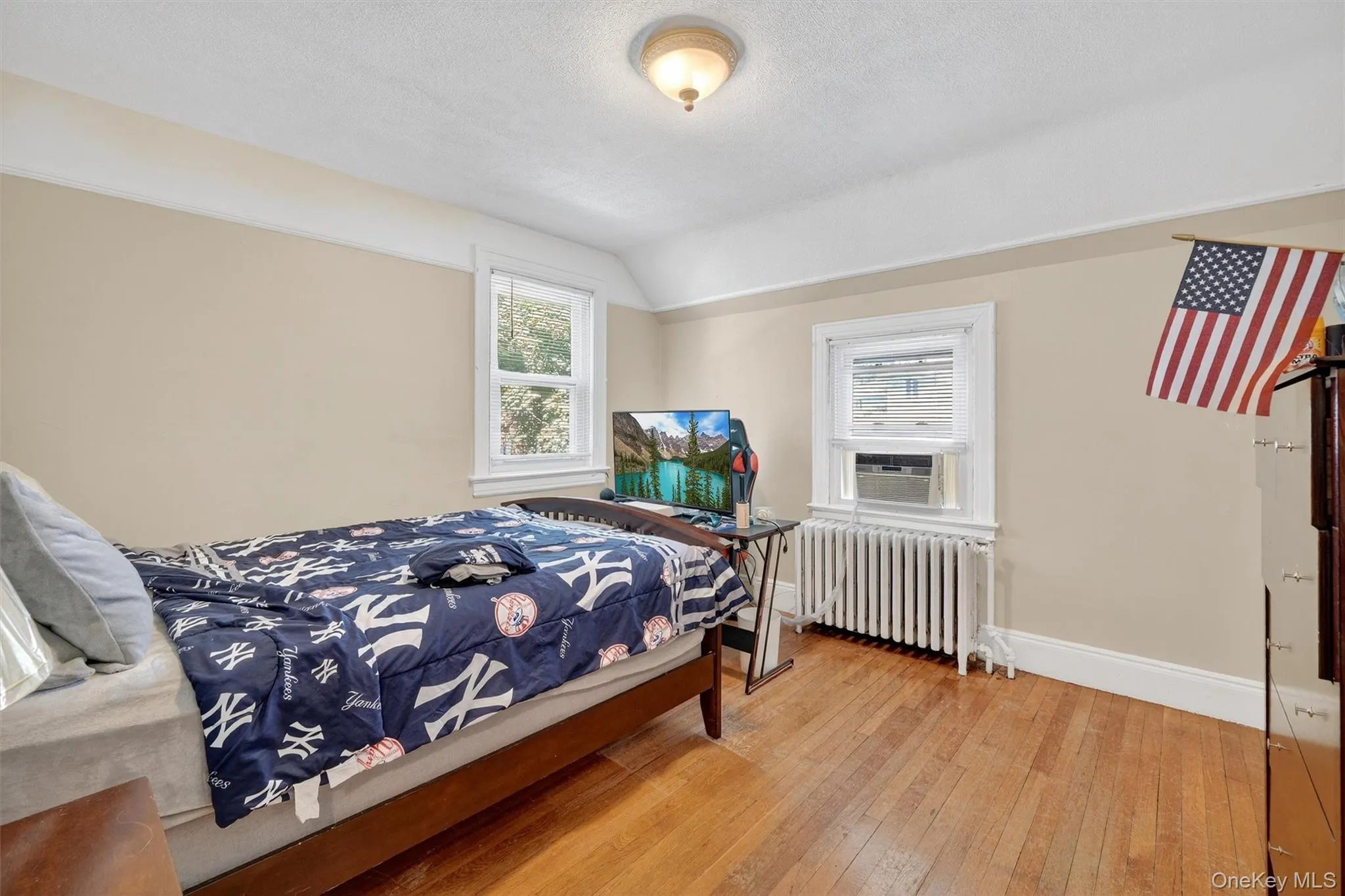 Bedroom with radiator heating unit, light wood finished floors, vaulted ceiling, and a textured ceiling Bedroom with radiator heating unit, light wood finished floors, vaulted ceiling, and a textured ceiling