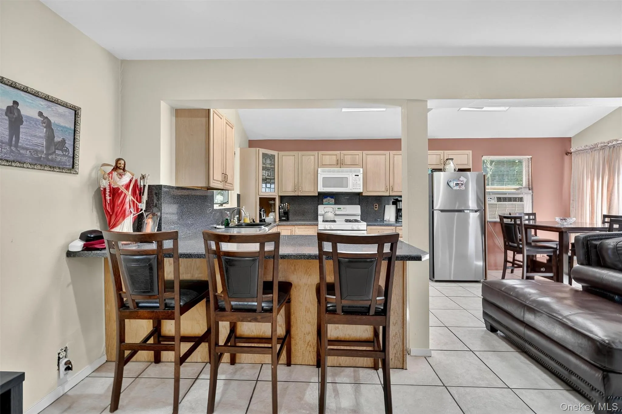 Kitchen featuring tasteful backsplash, light brown cabinets, white appliances, a kitchen bar, and dark countertops Kitchen featuring tasteful backsplash, light brown cabinets, white appliances, a kitchen bar, and dark countertops